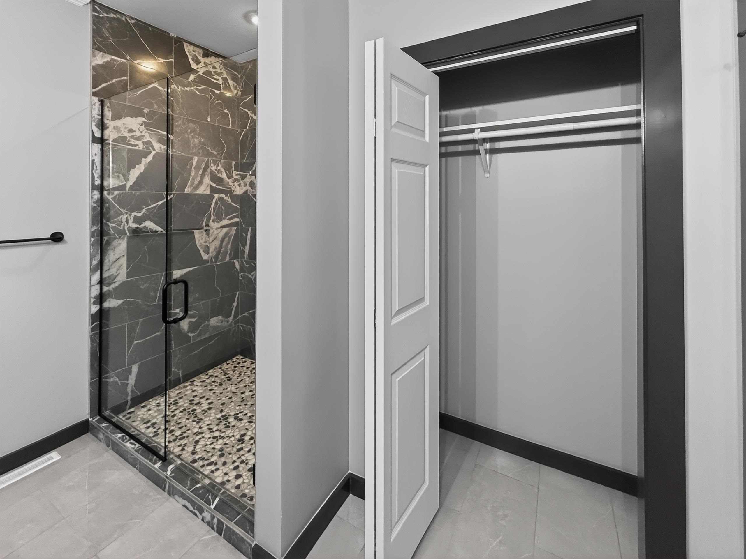 Glass-enclosed shower featuring dark stone-patterned tile, pebble flooring, and black hardware