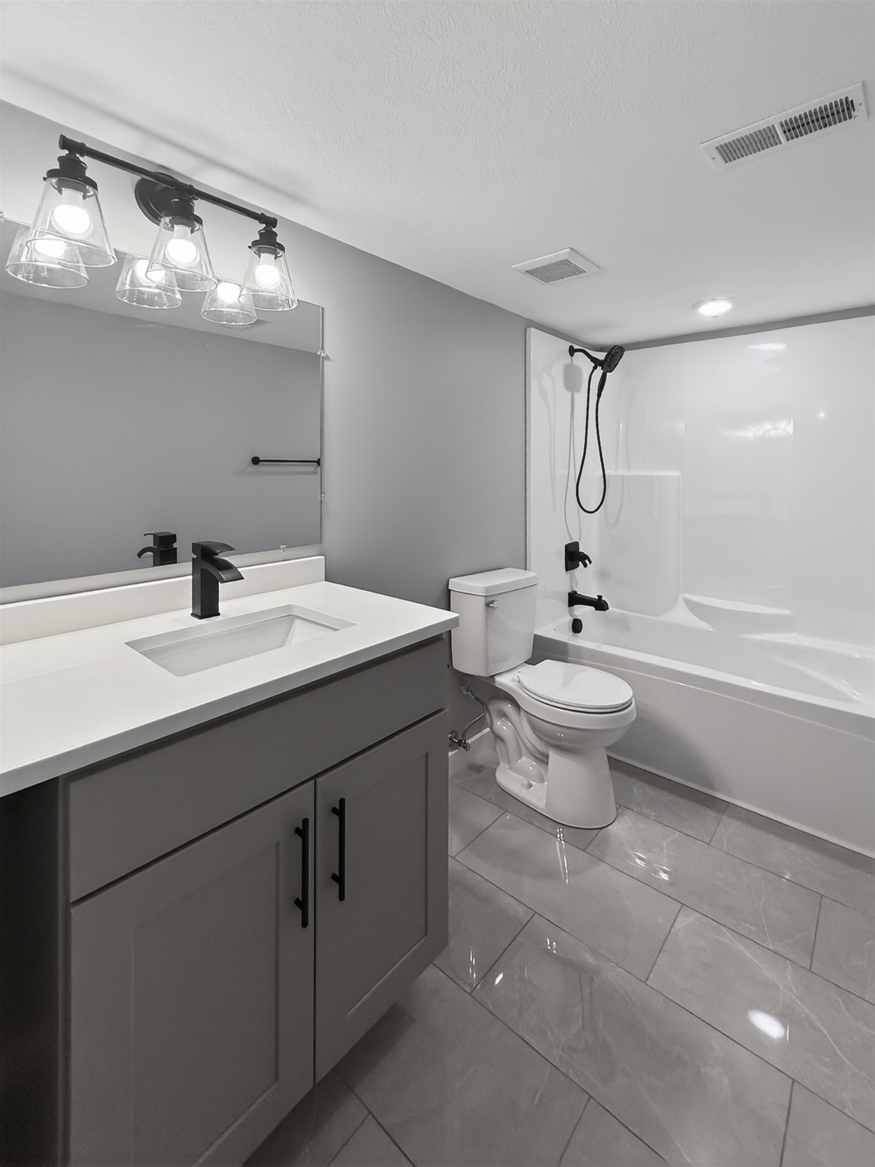 Full bathroom featuring a single vanity with a white countertop and gray cabinetry, a white toilet, and a white tub with a shower fixture
