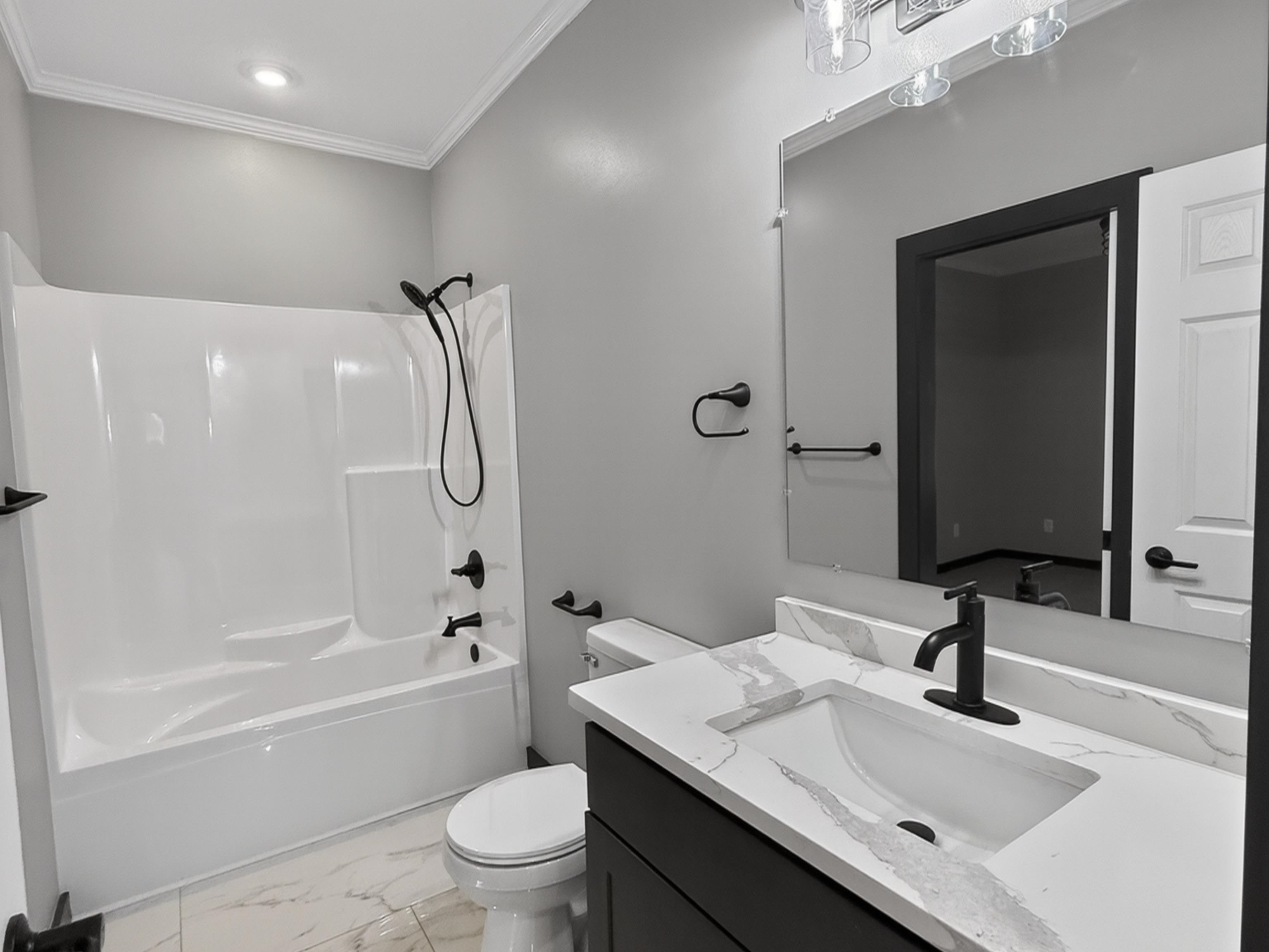 Bathroom featuring a white tub/shower combination with matte black fixtures, a dark vanity cabinet with a white countertop and integrated sink, a rectangular mirror, and white tile flooring