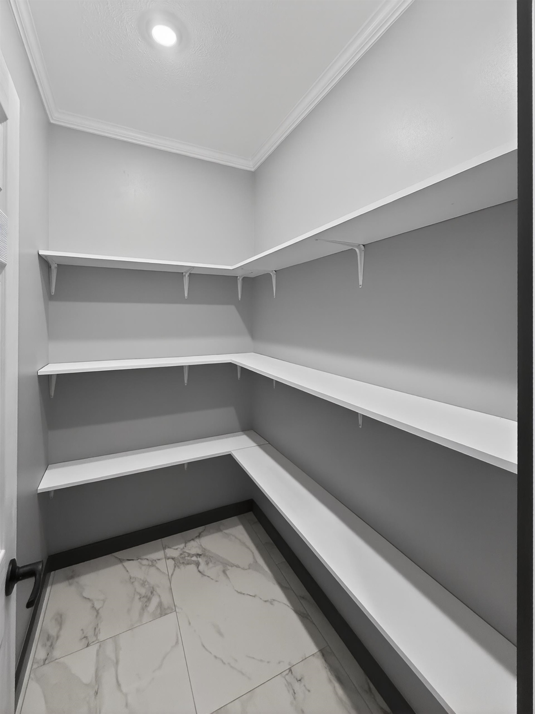 Spacious pantry featuring multiple tiers of white shelving, marble-look tile flooring, and recessed ceiling lighting