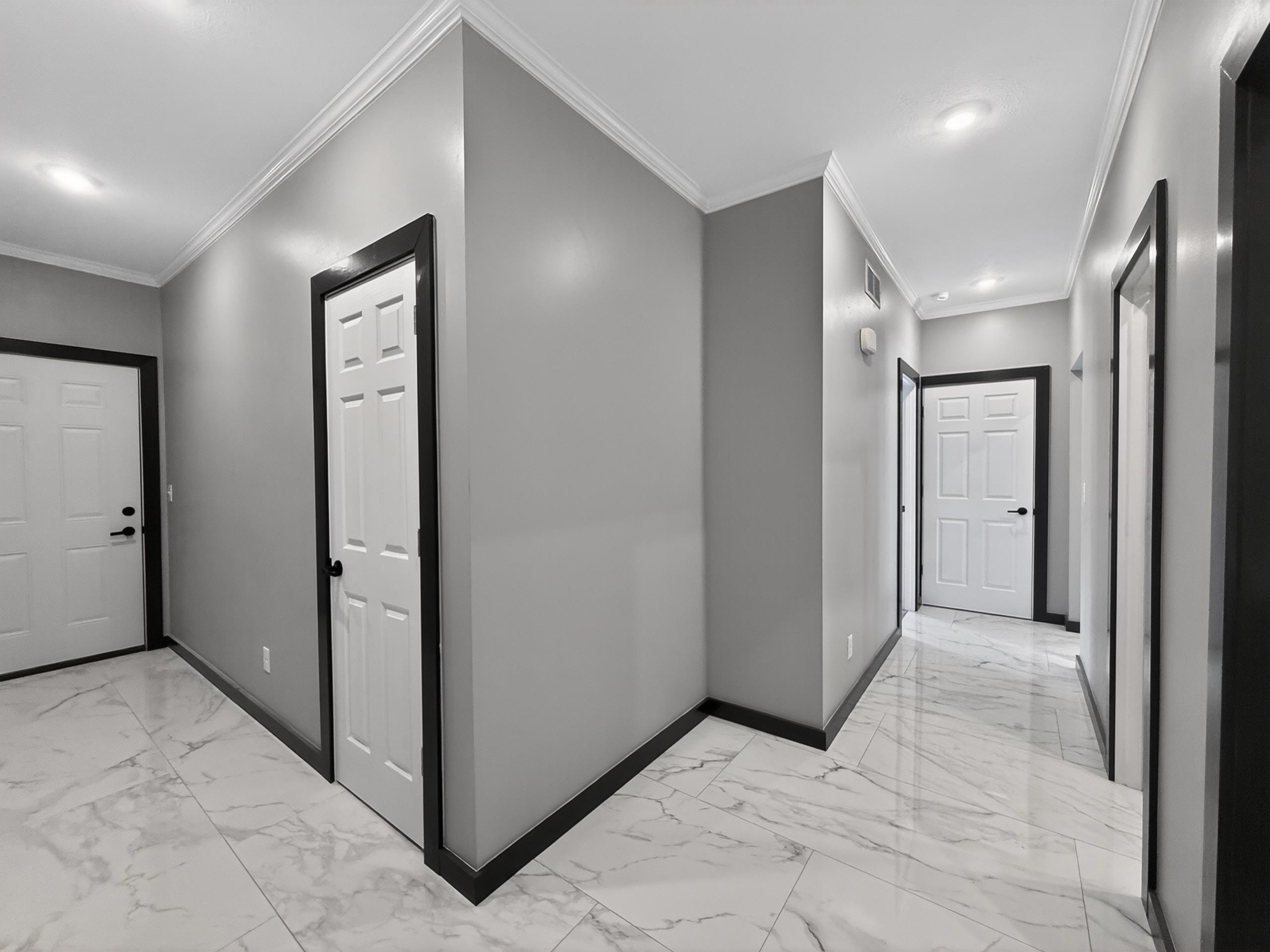 Hallway featuring light gray walls, dark trim accents, white panel doors, recessed lighting, and large format marble-look tile flooring