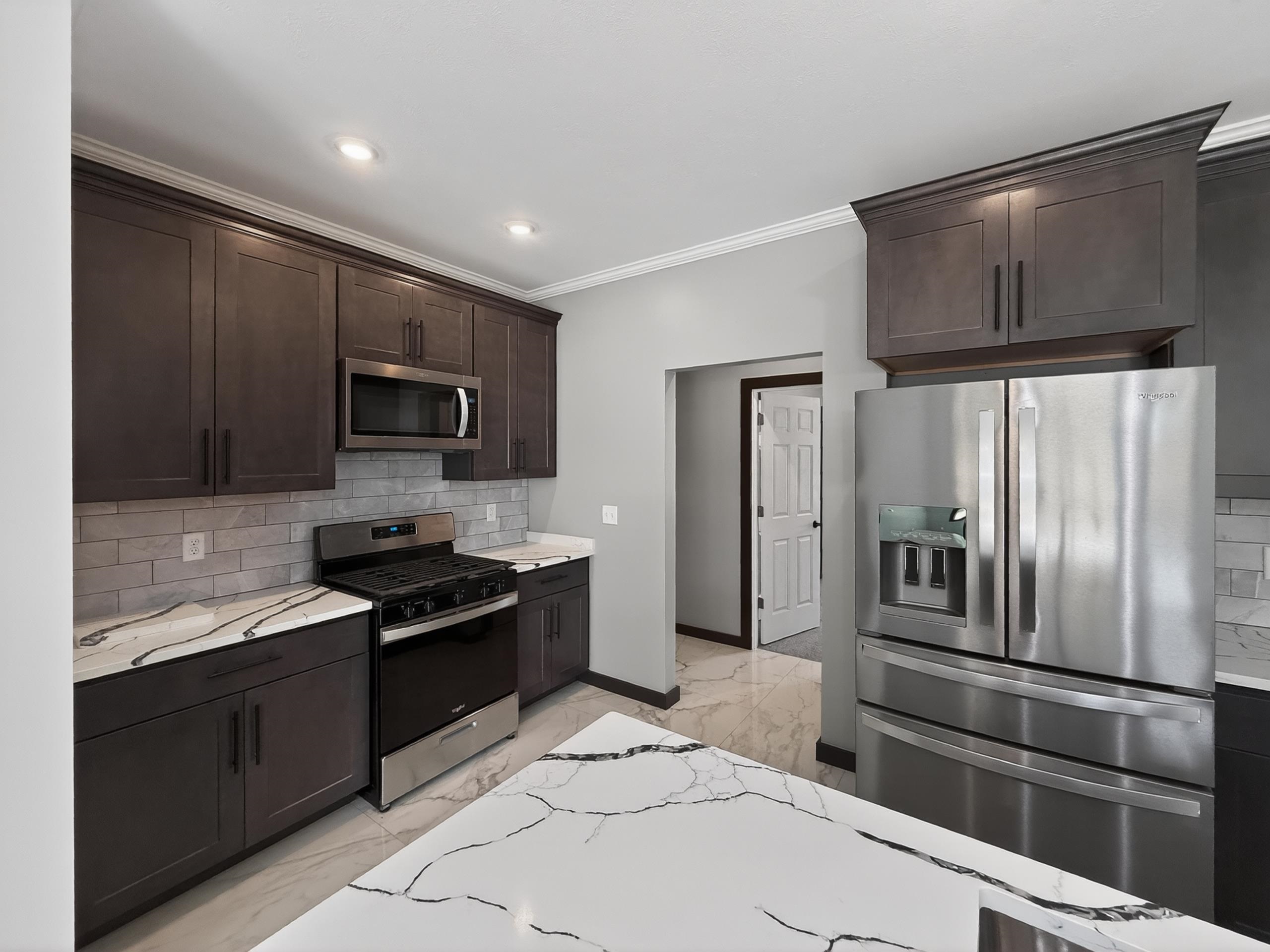 Modern kitchen featuring dark wood-finish cabinetry, stainless steel appliances, white countertops with black veining, gray subway tile backsplash, and recessed lighting