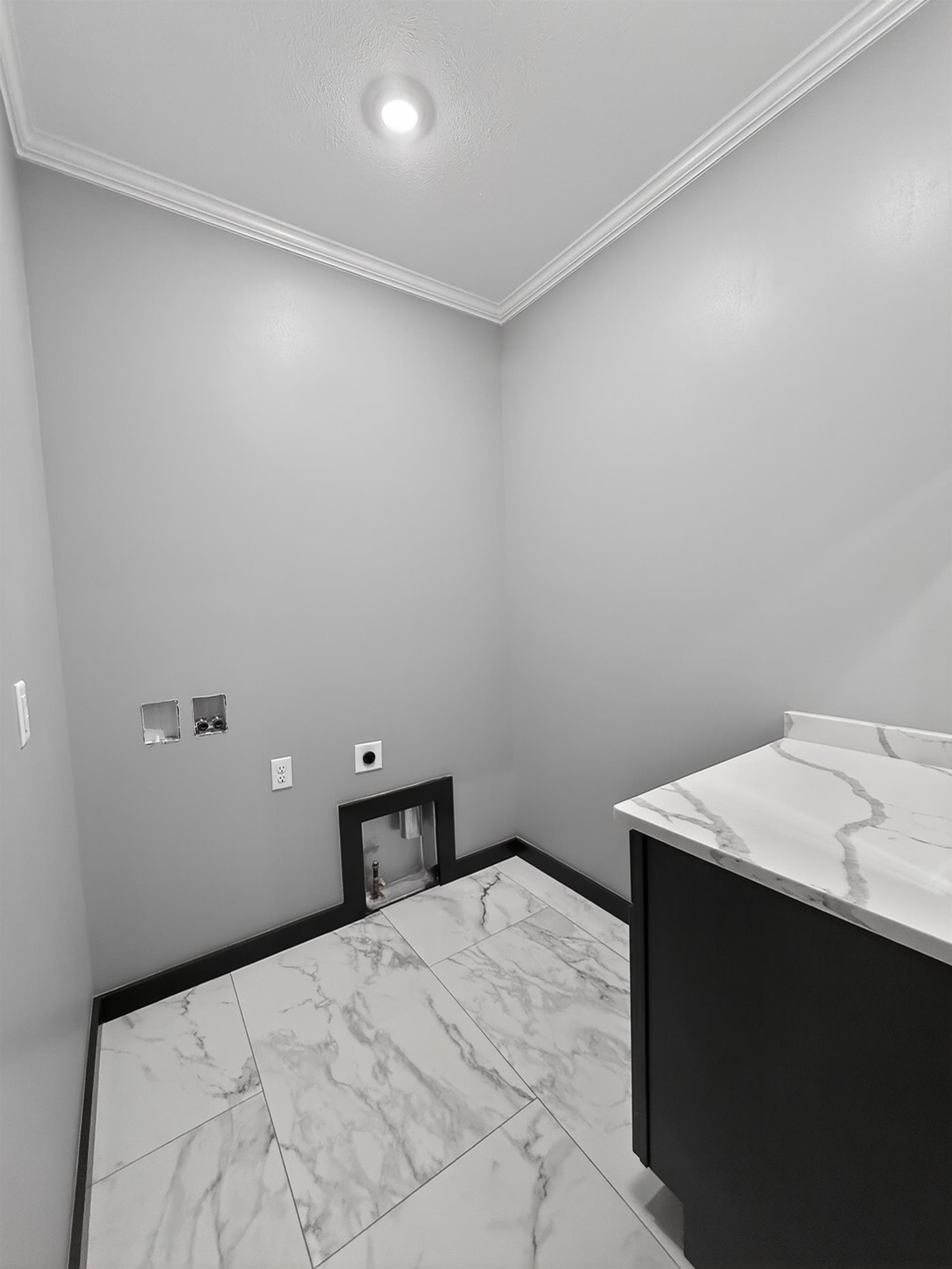 Dedicated utility room featuring large format marble-look tile flooring, crown molding, and a built-in counter with a complementary marble-look surface