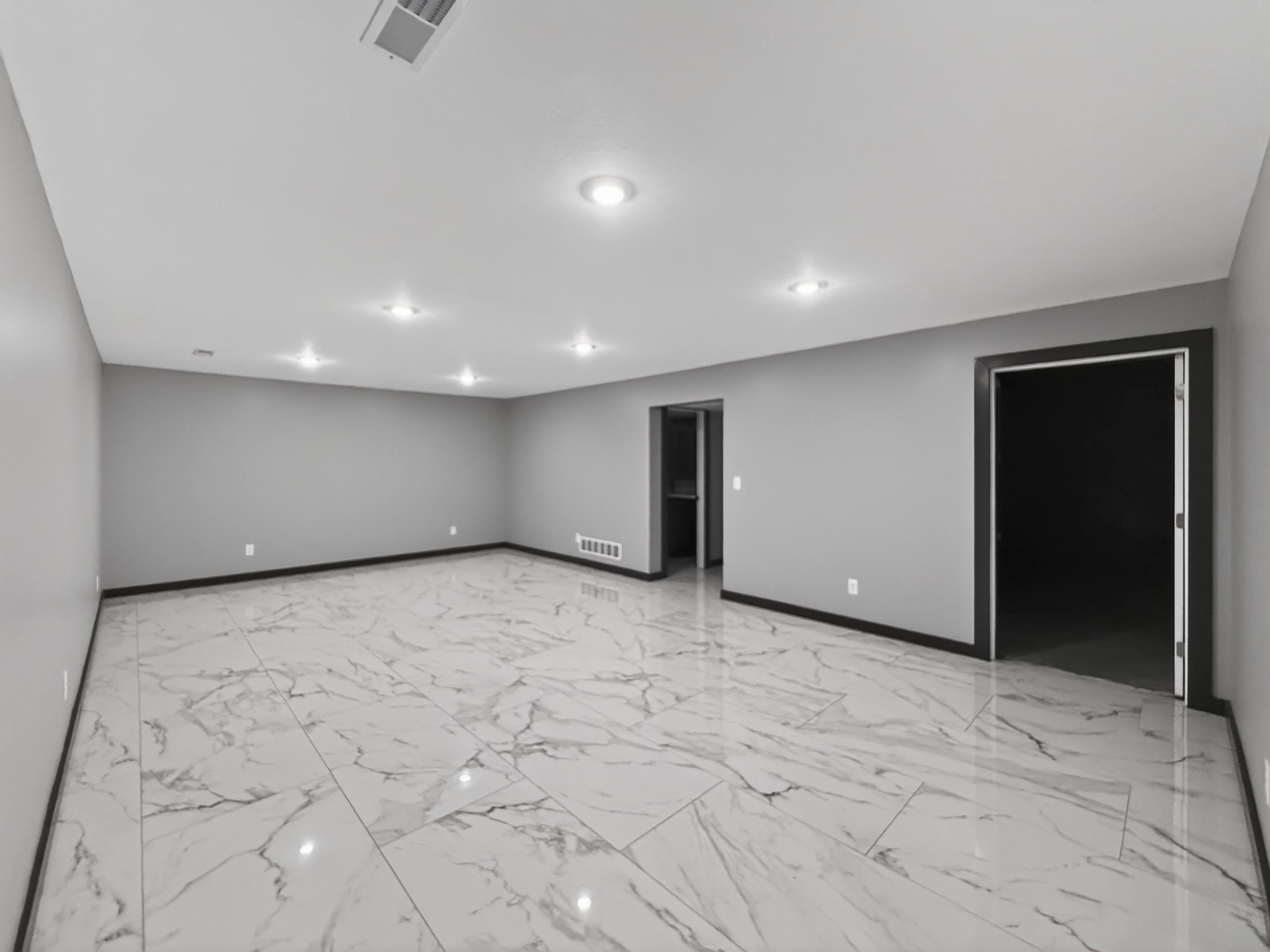 Spacious interior room featuring large format white and grey patterned floor tiles, recessed ceiling lighting, and two doorways with dark trim