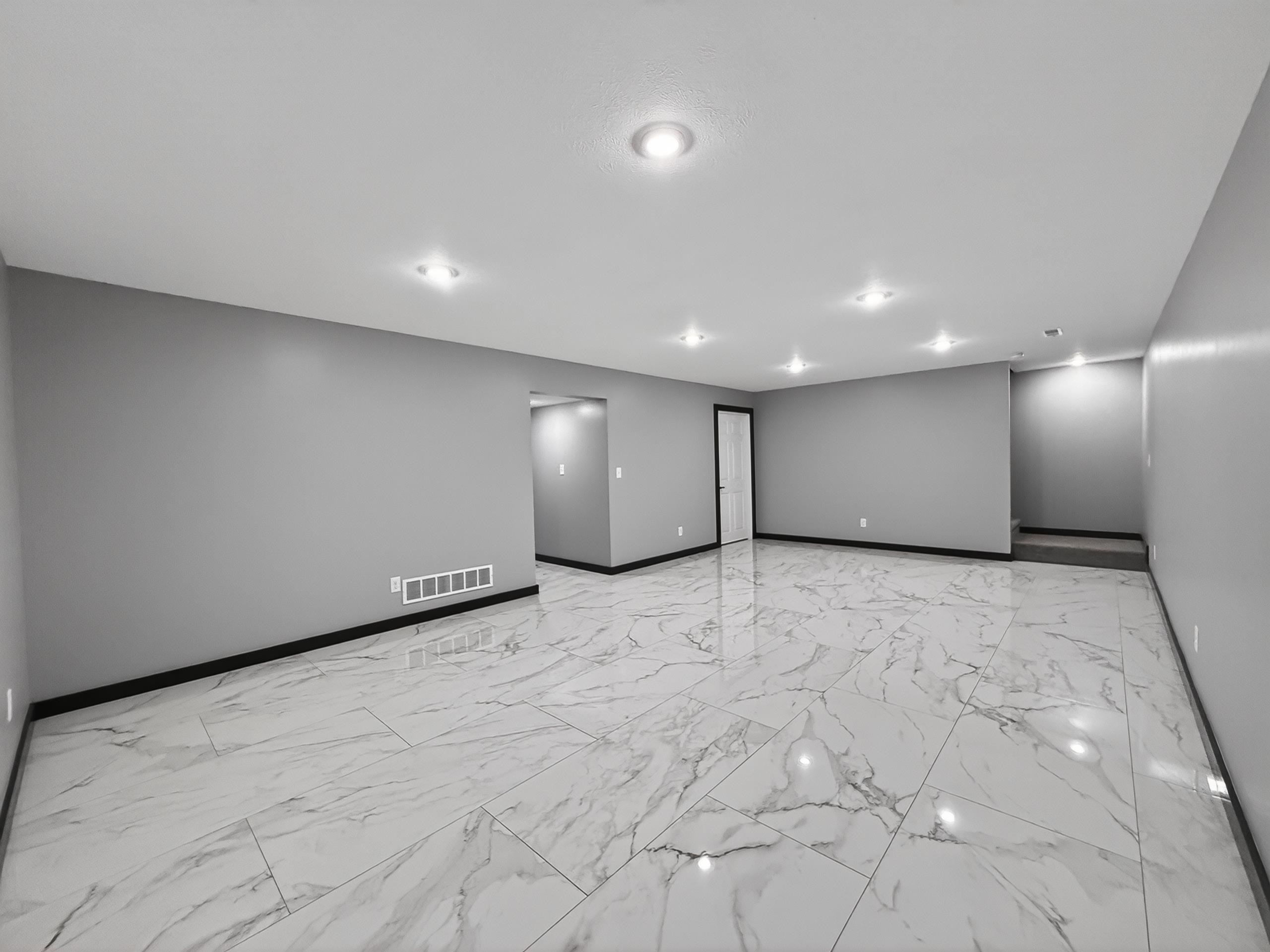 Spacious interior featuring large format marble-look tile flooring, recessed ceiling lighting, light gray painted walls, and dark trim