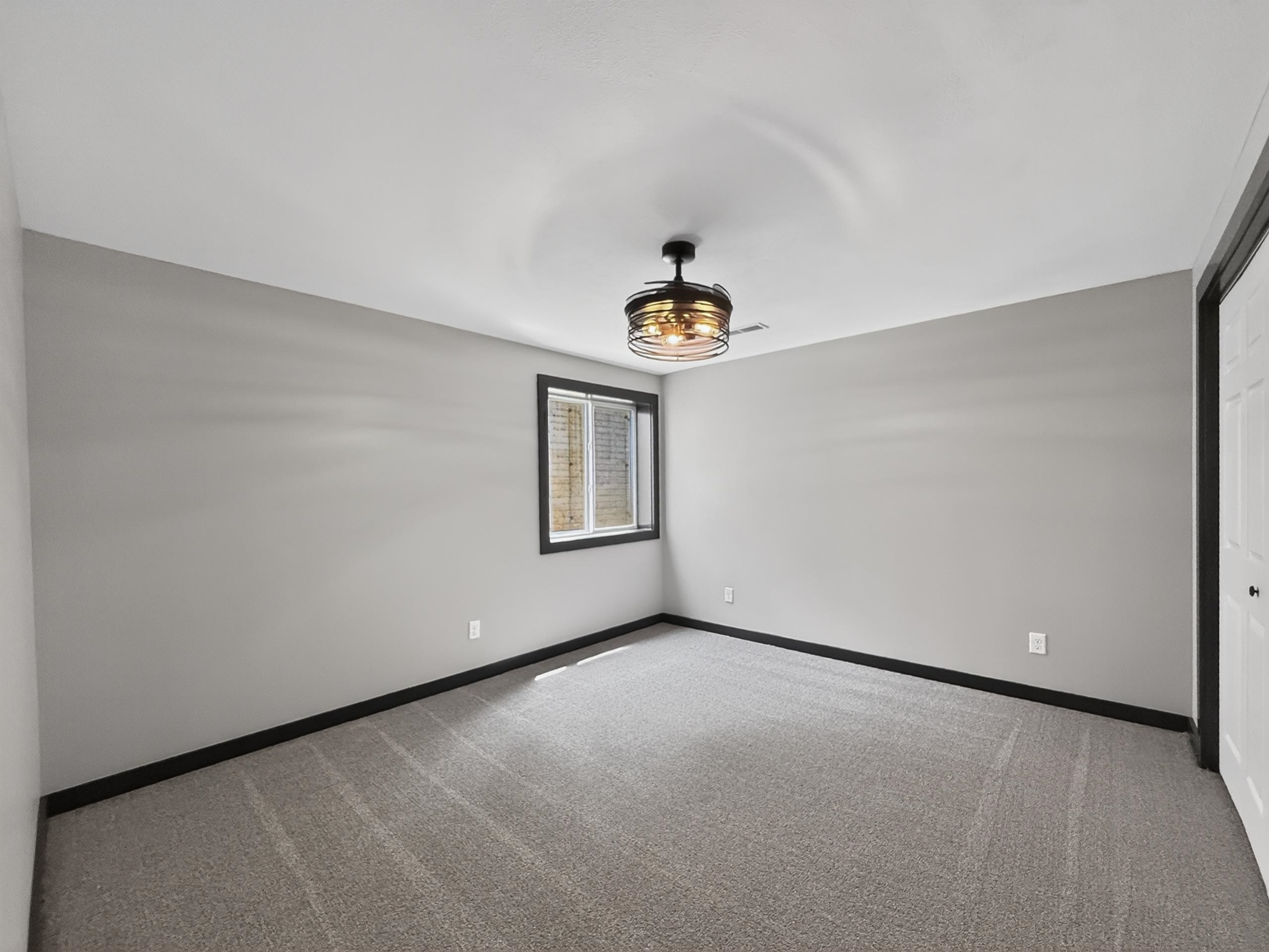 Neutral-toned room featuring a window with dark trim, a decorative ceiling fan with an industrial cage design, and plush gray carpeting