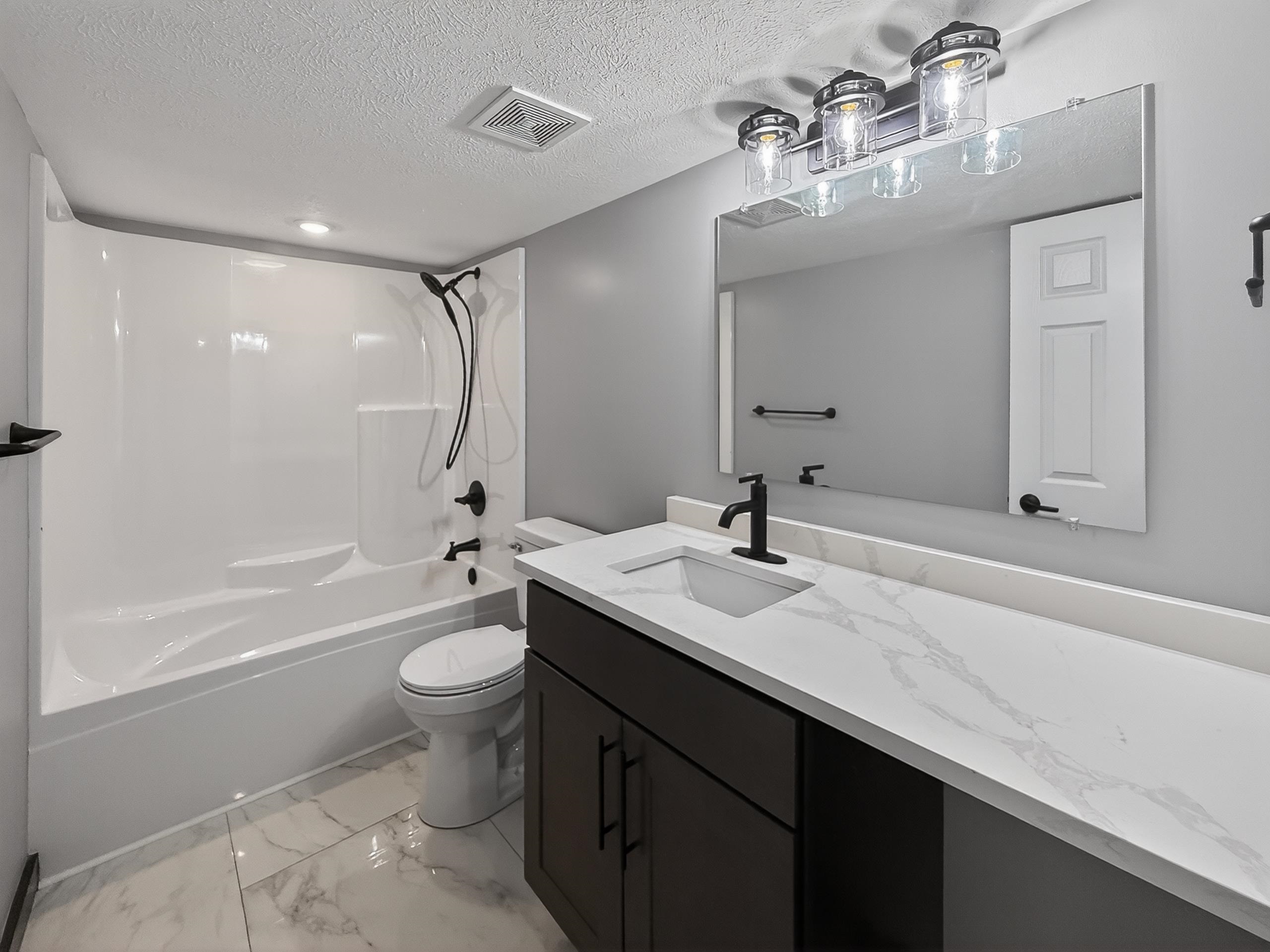 Bathroom featuring a white bathtub and shower surround with matte black fixtures