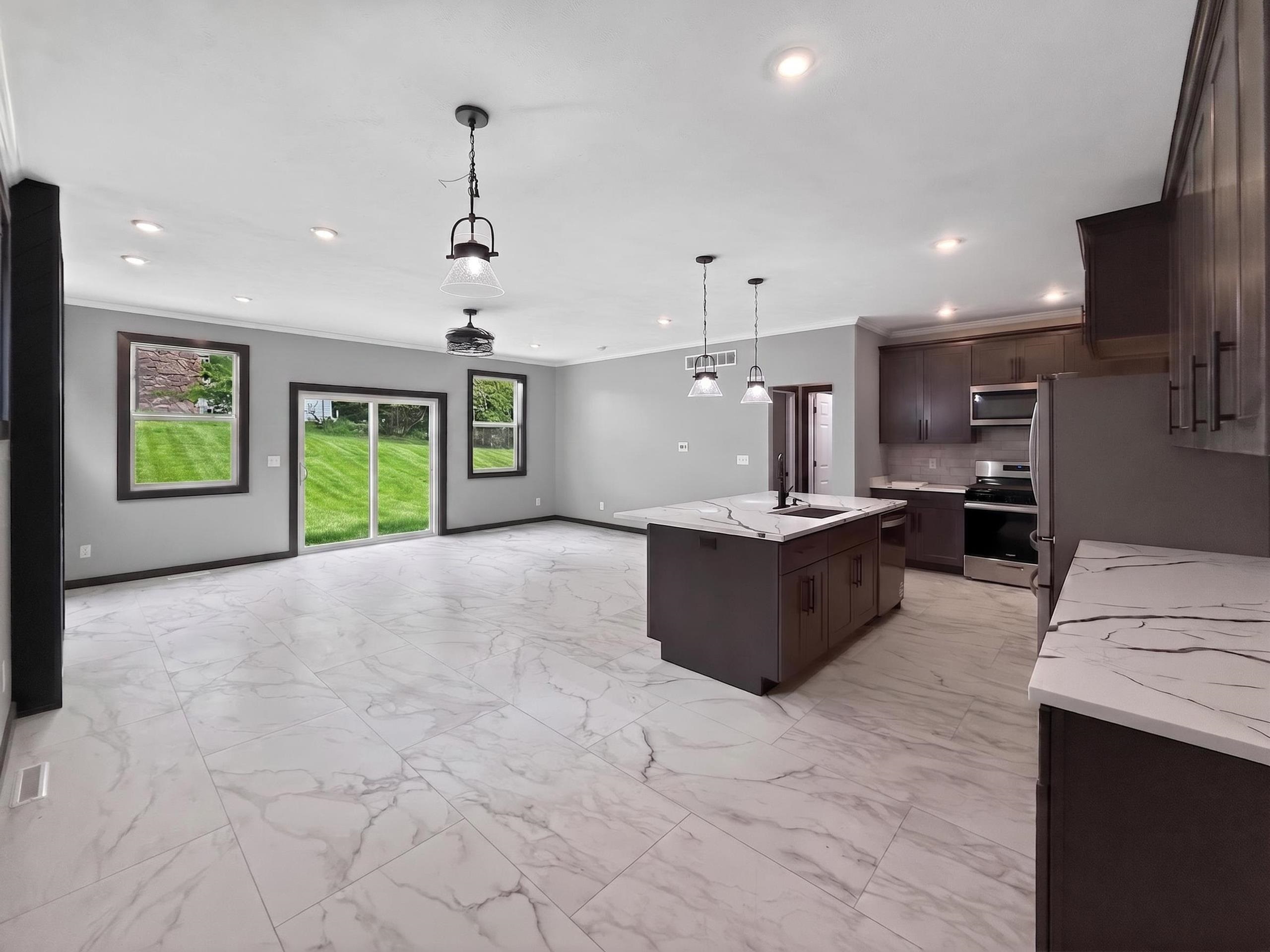 Open-concept living space featuring marble-look tile flooring, a modern kitchen island with an undermount sink, dark wood-finish cabinetry, stainless steel appliances, and a sliding glass door to the exterior