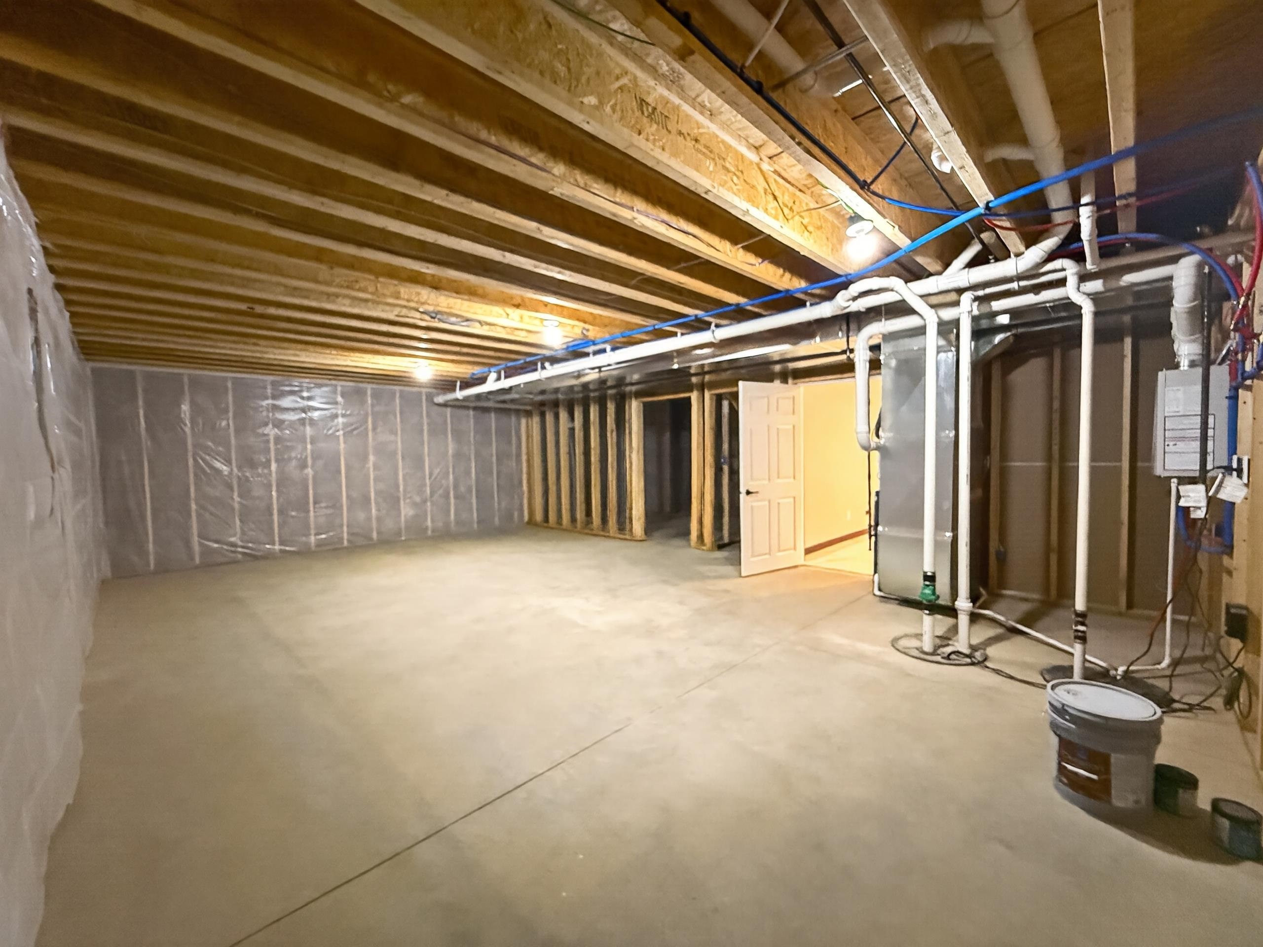 Unfinished basement featuring exposed wood joists, concrete flooring, perimeter wall framing with insulation, and visible utility lines