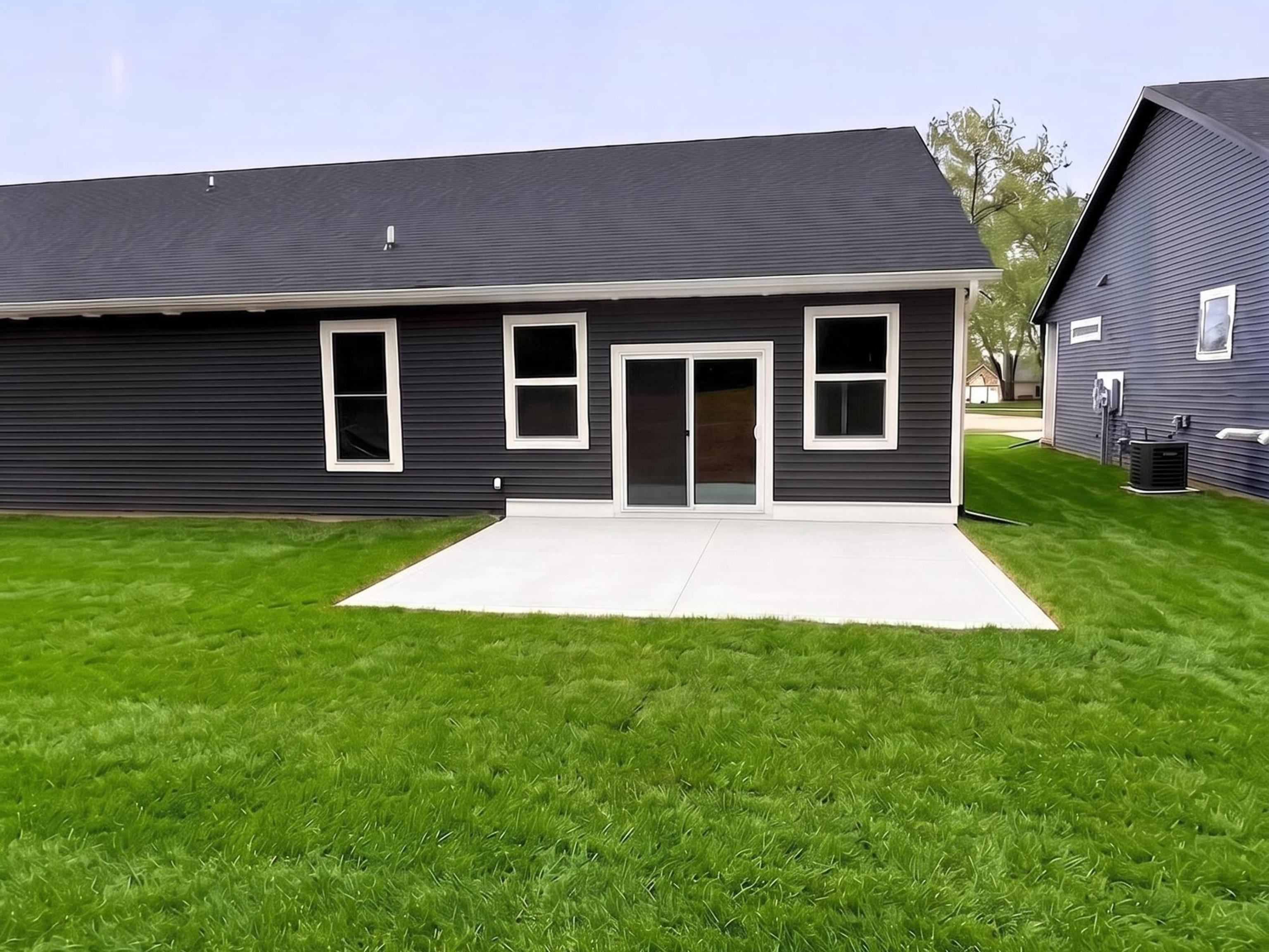 Rear exterior featuring dark siding, white trim windows, a concrete patio, and a sliding glass door