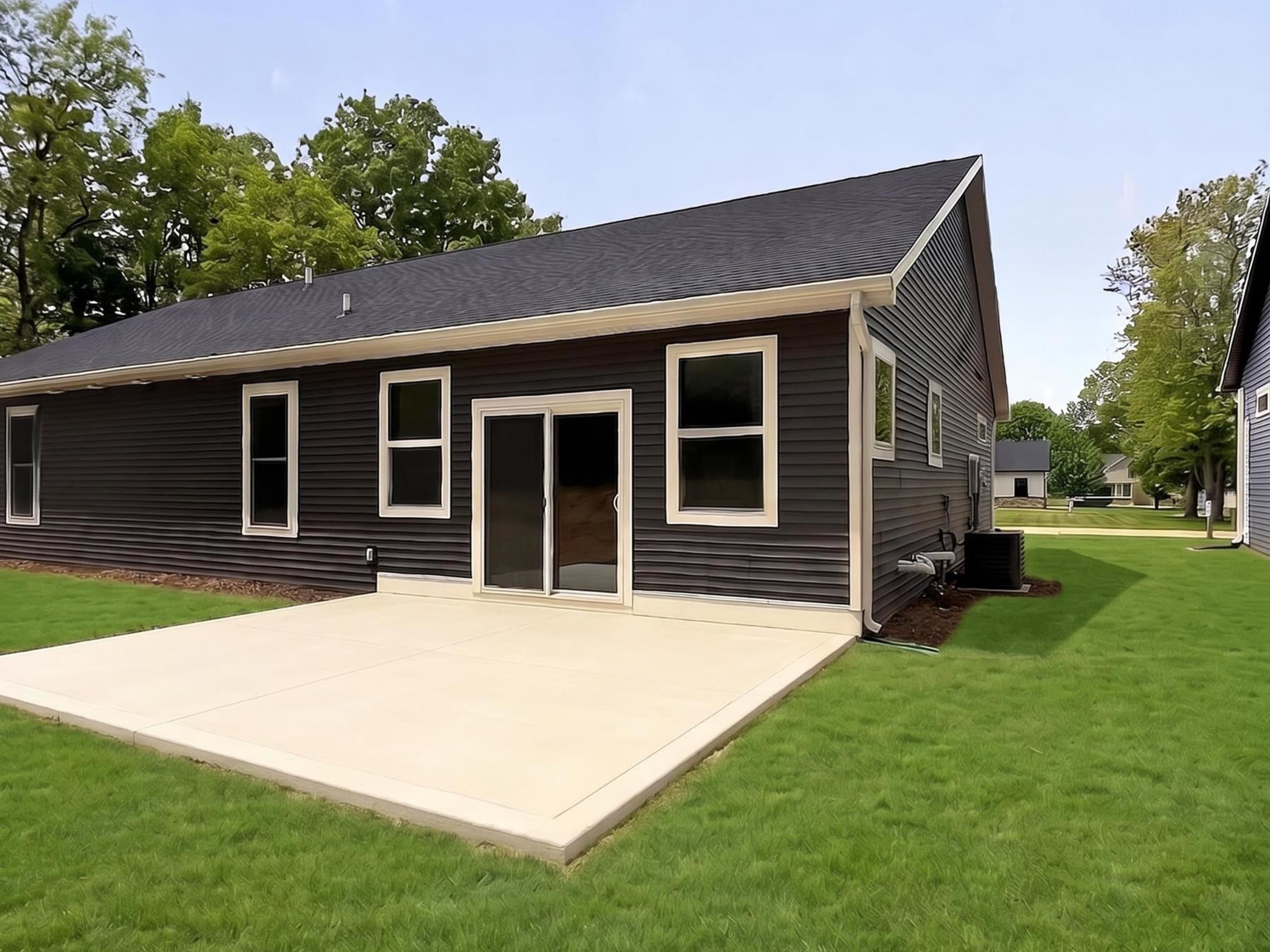 Expansive concrete patio with direct access via sliding glass doors to the home, featuring dark horizontal siding, white trim windows, and a dark shingle roof