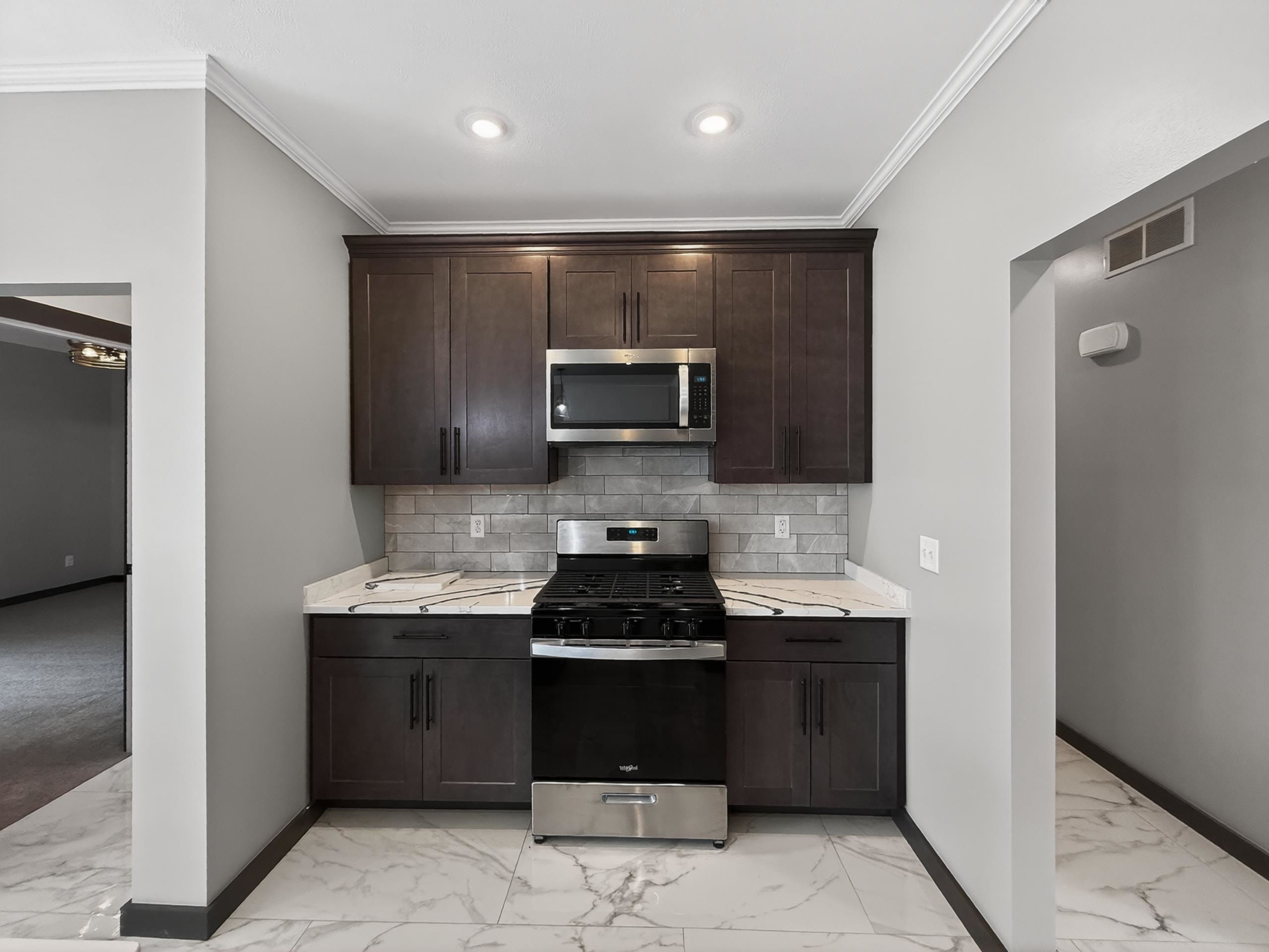 Kitchen featuring dark wood-finish cabinetry, stainless steel appliances, a subway tile backsplash, and light-toned countertops