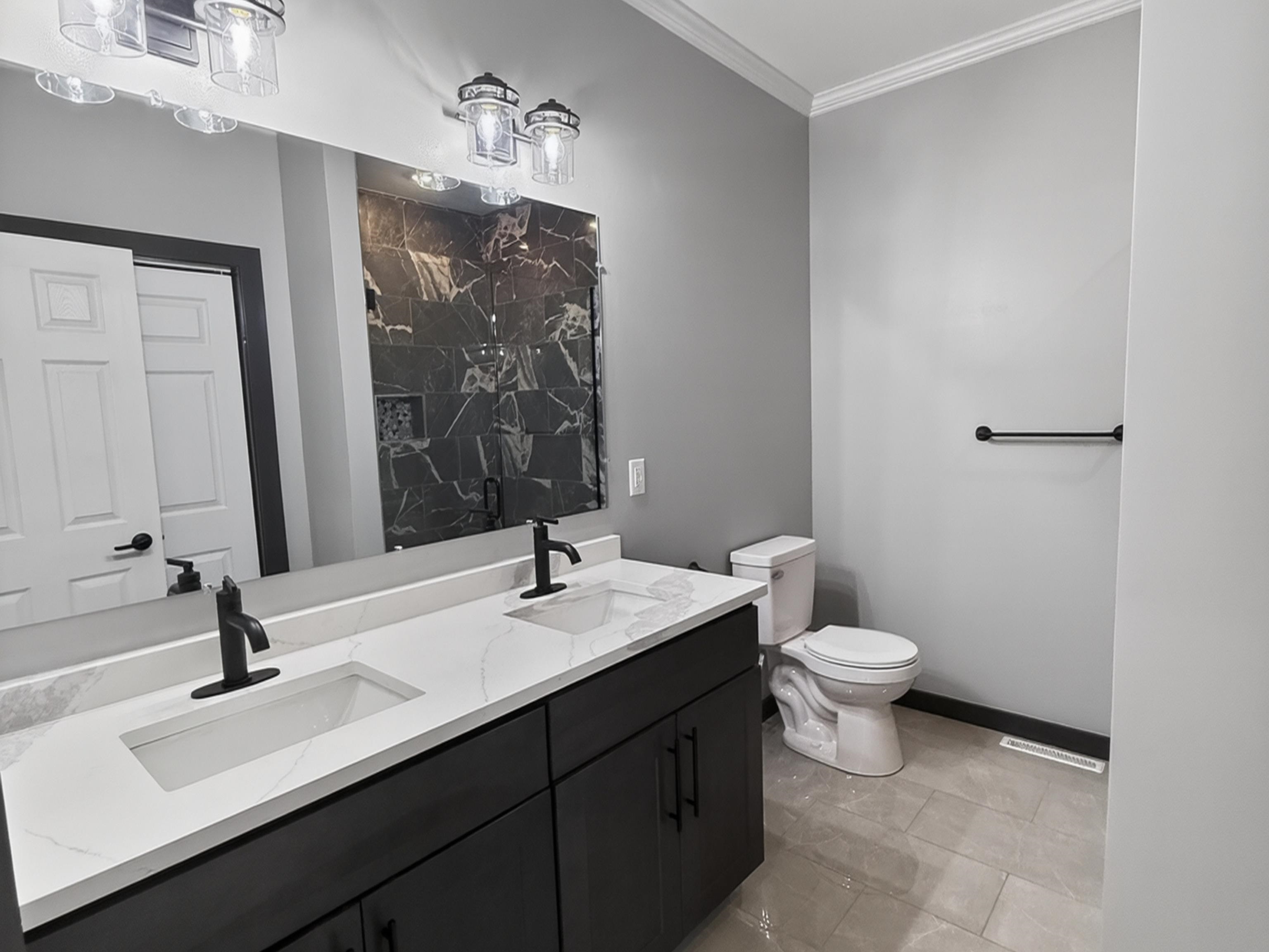 Bathroom featuring a dual-sink vanity with white countertops, matte black faucets, and dark cabinetry