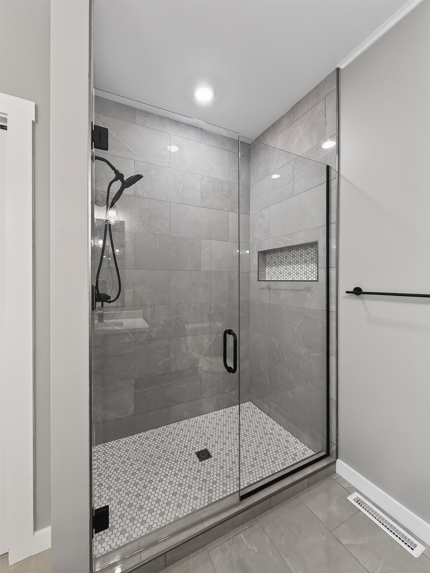Contemporary shower enclosure featuring a frameless glass door, matte black hardware, large format grey wall tiles, a mosaic tile shower pan, and a recessed shower niche