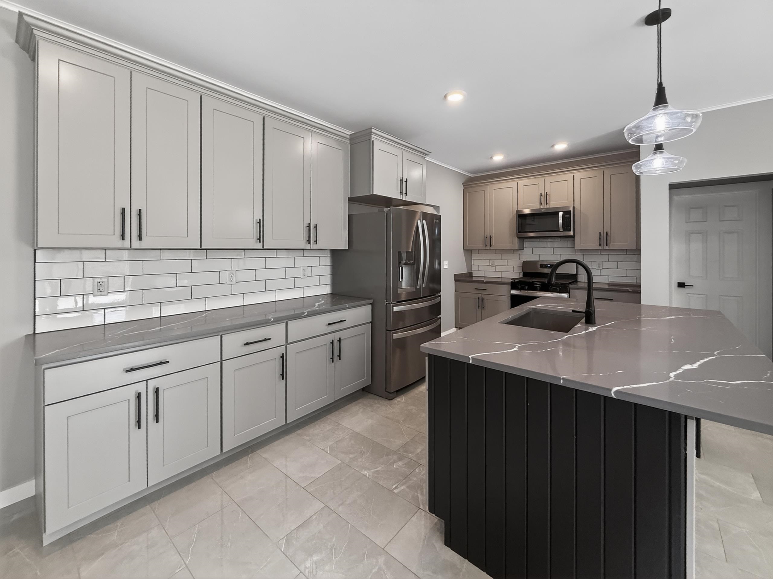 Modern kitchen featuring an island with integrated sink, two-tone cabinetry, stainless steel appliances, subway tile backsplash, and stone countertops