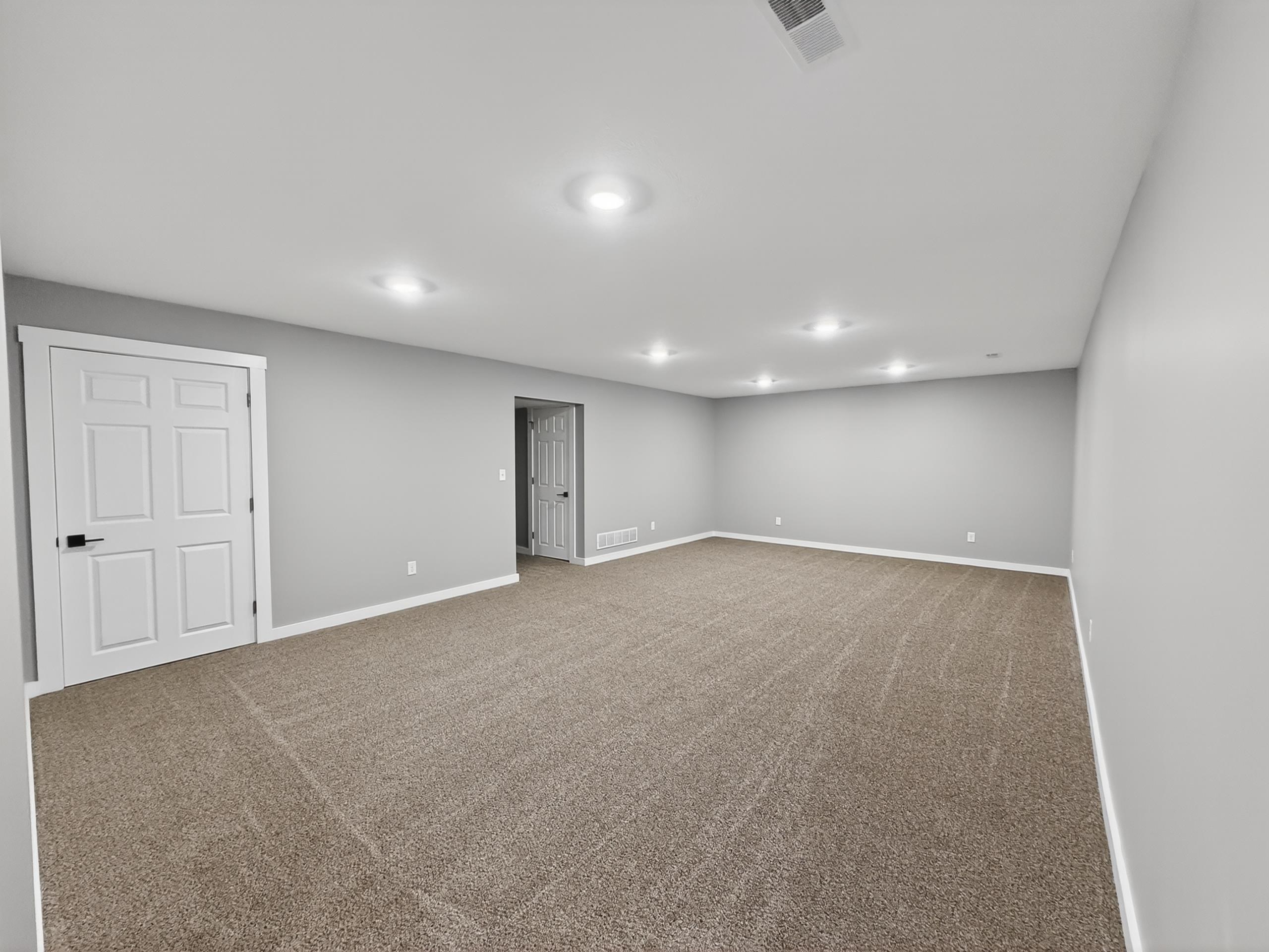 Spacious room featuring neutral carpeting, light gray wall tones, white trim, and recessed ceiling lighting
