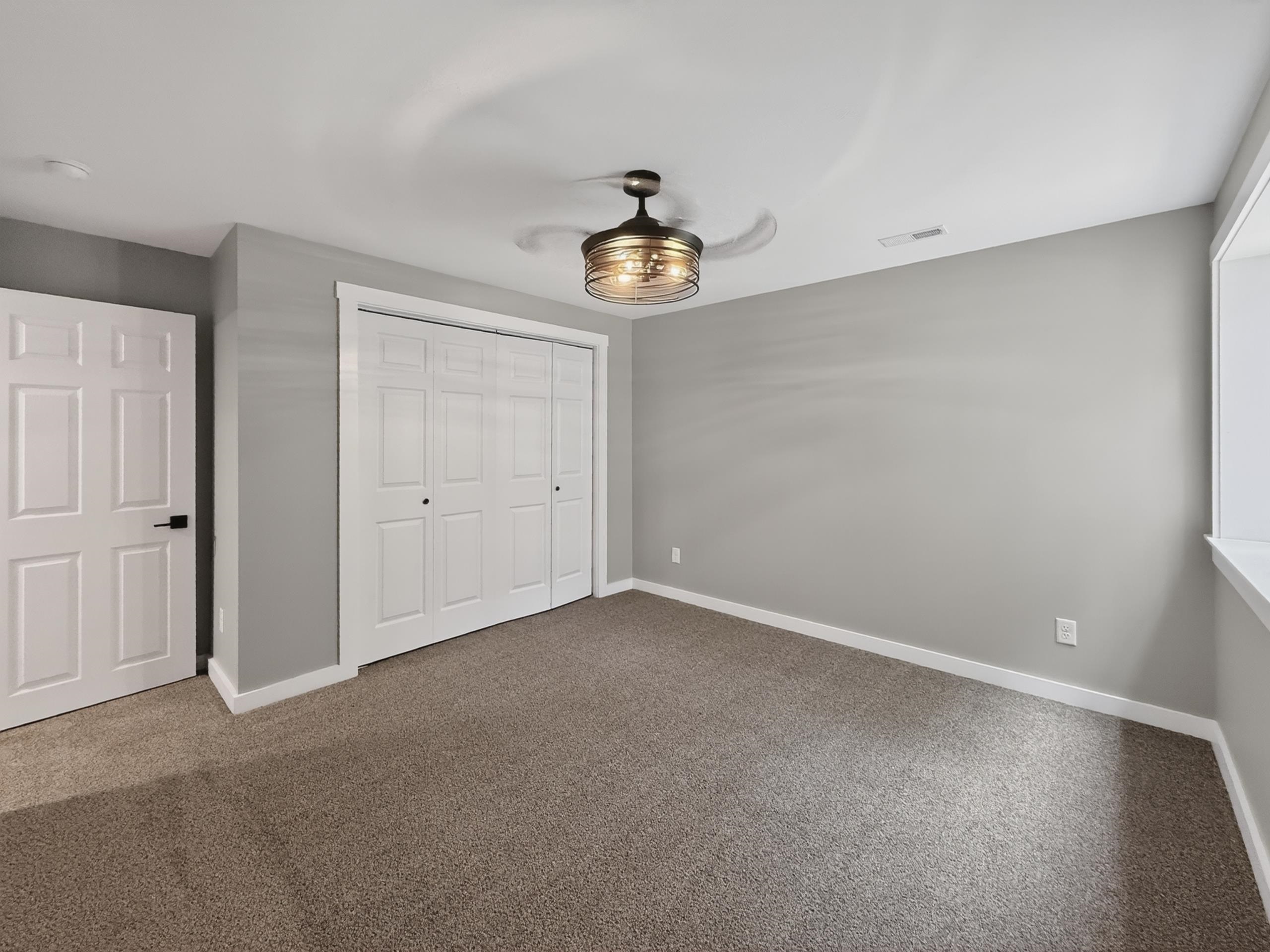 Neutral-toned room featuring a ceiling fan with integrated lighting, textured carpet flooring, and a window opening with a white sill