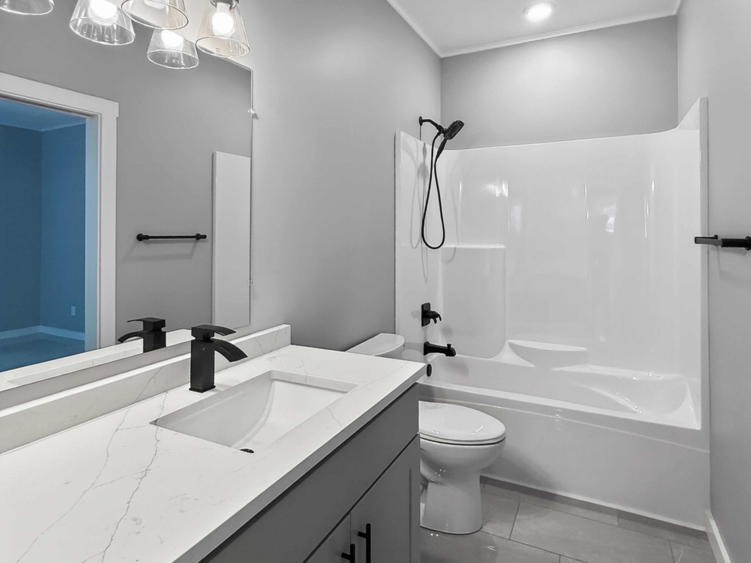 Bathroom featuring a white bathtub with shower surround, matte black fixtures, a white vanity countertop with an integrated sink, a large wall-mounted mirror, and tile flooring