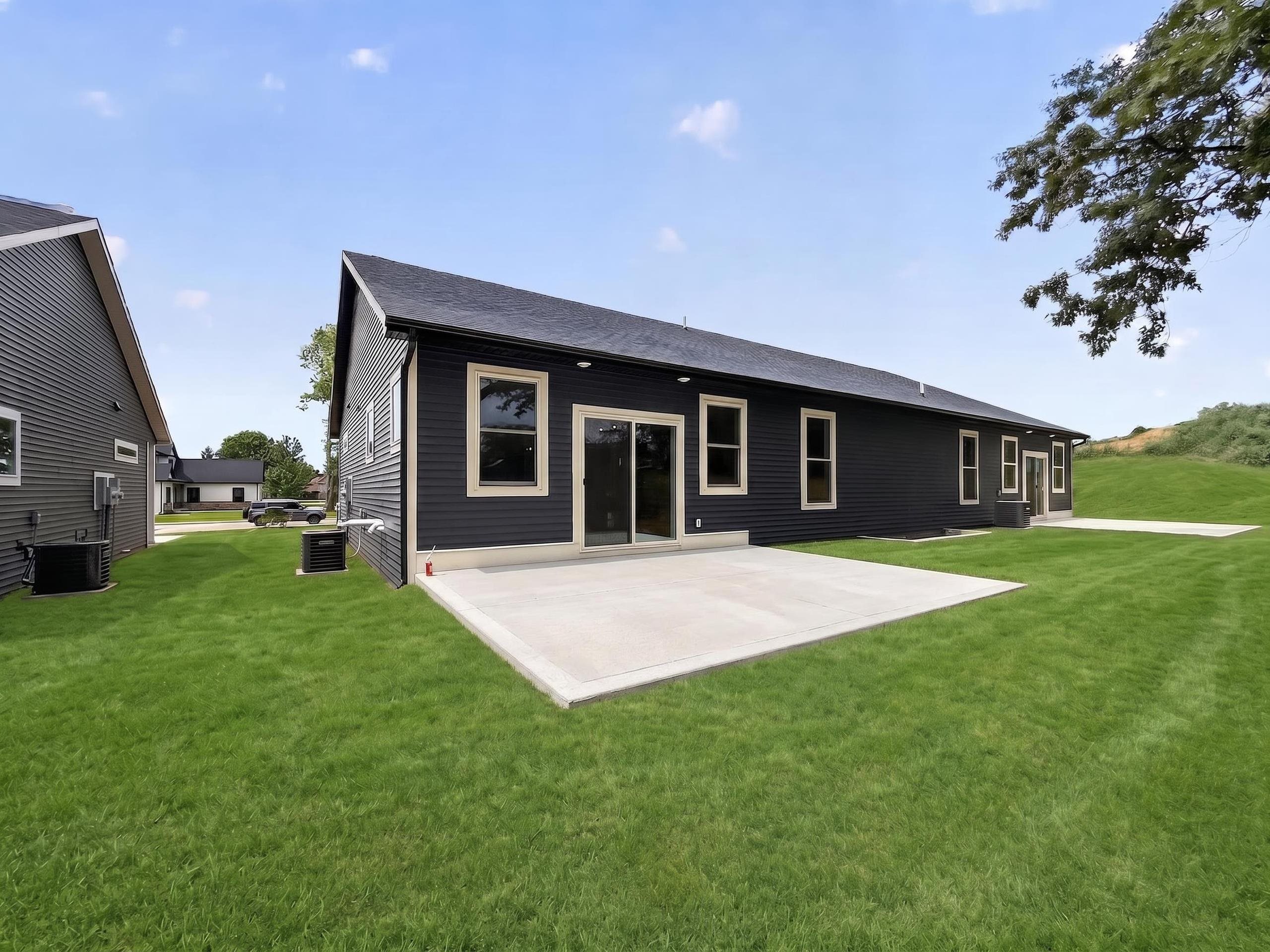 Rear exterior featuring dark horizontal siding, multiple windows with light trim, and a concrete patio