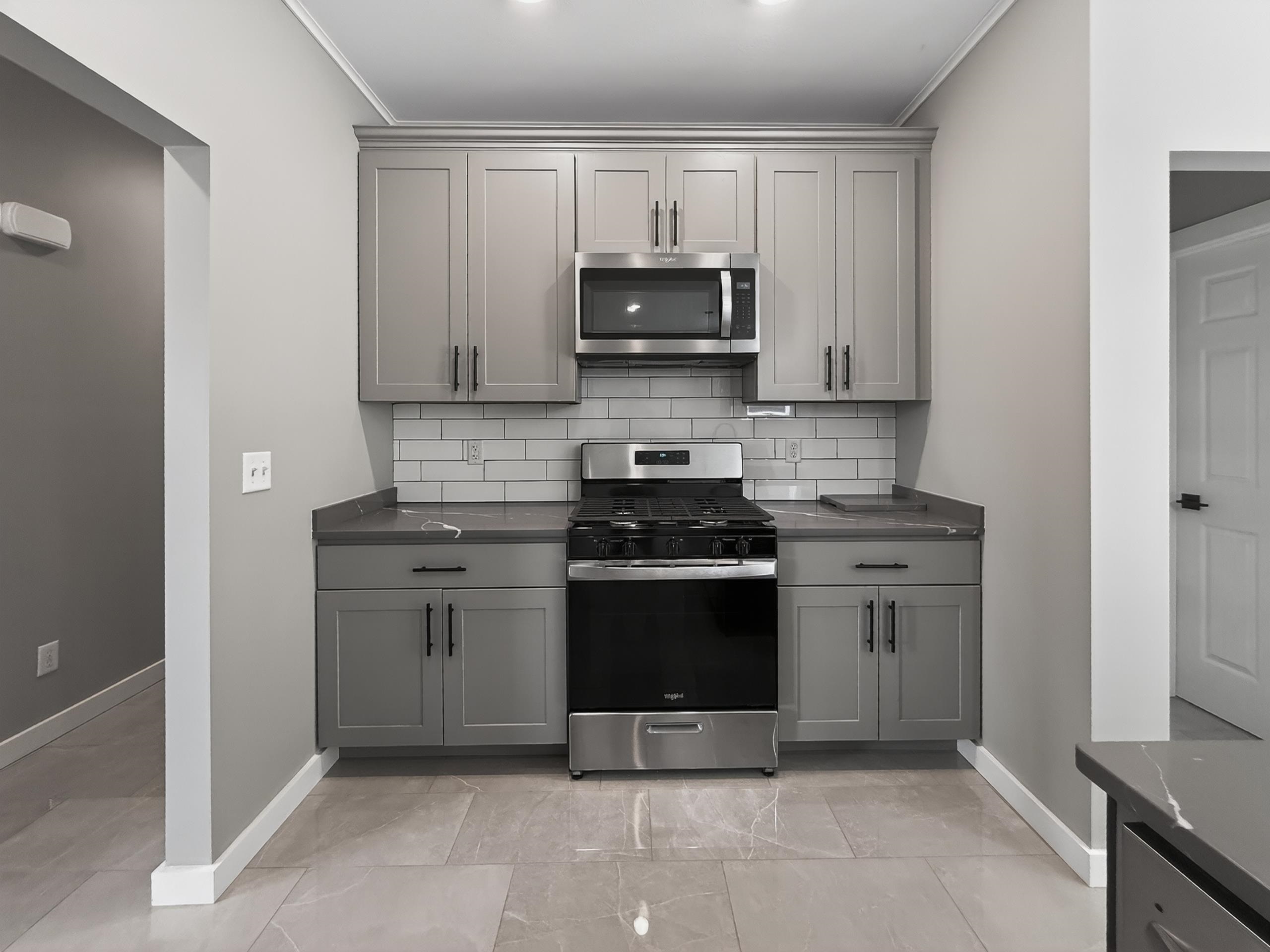 Contemporary kitchen with grey shaker-style cabinetry, stainless steel appliances, grey countertop, and subway tile backsplash