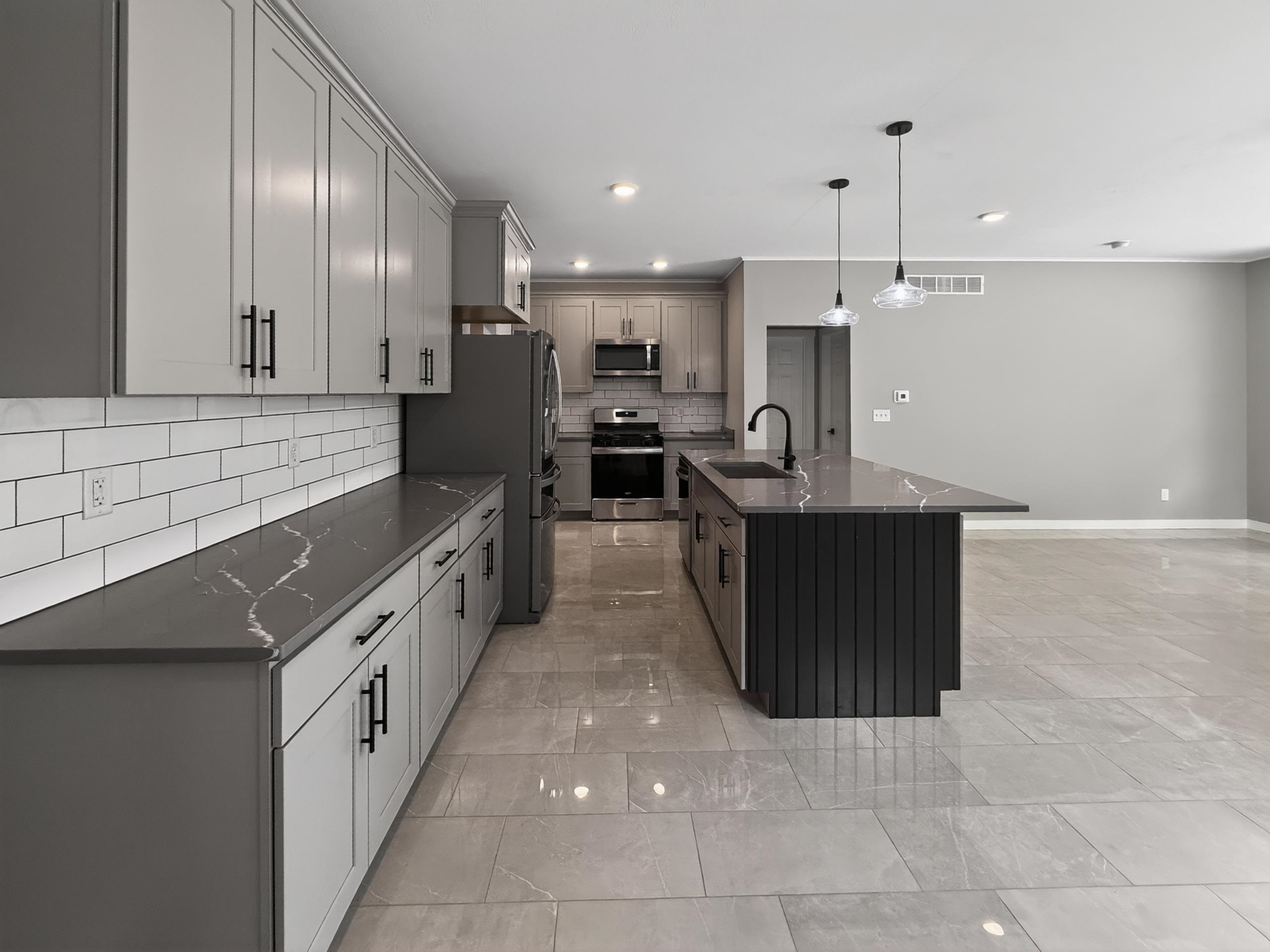 Modern kitchen featuring light gray cabinetry, quartz countertops with subtle veining, and a contrasting dark gray island with vertical paneling