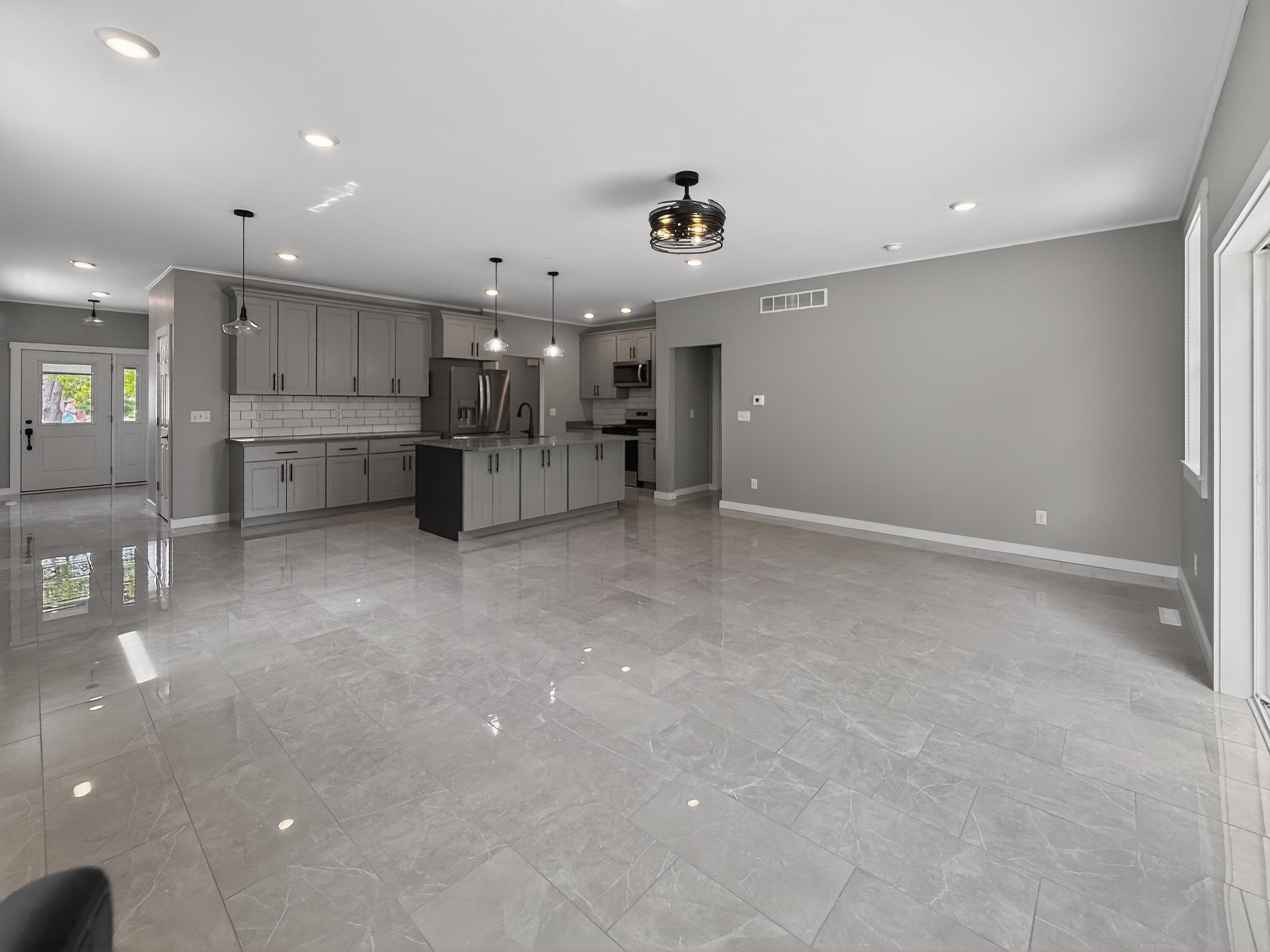 Open-concept living space featuring sleek gray cabinetry, a central island with pendant lighting, and stainless steel appliances