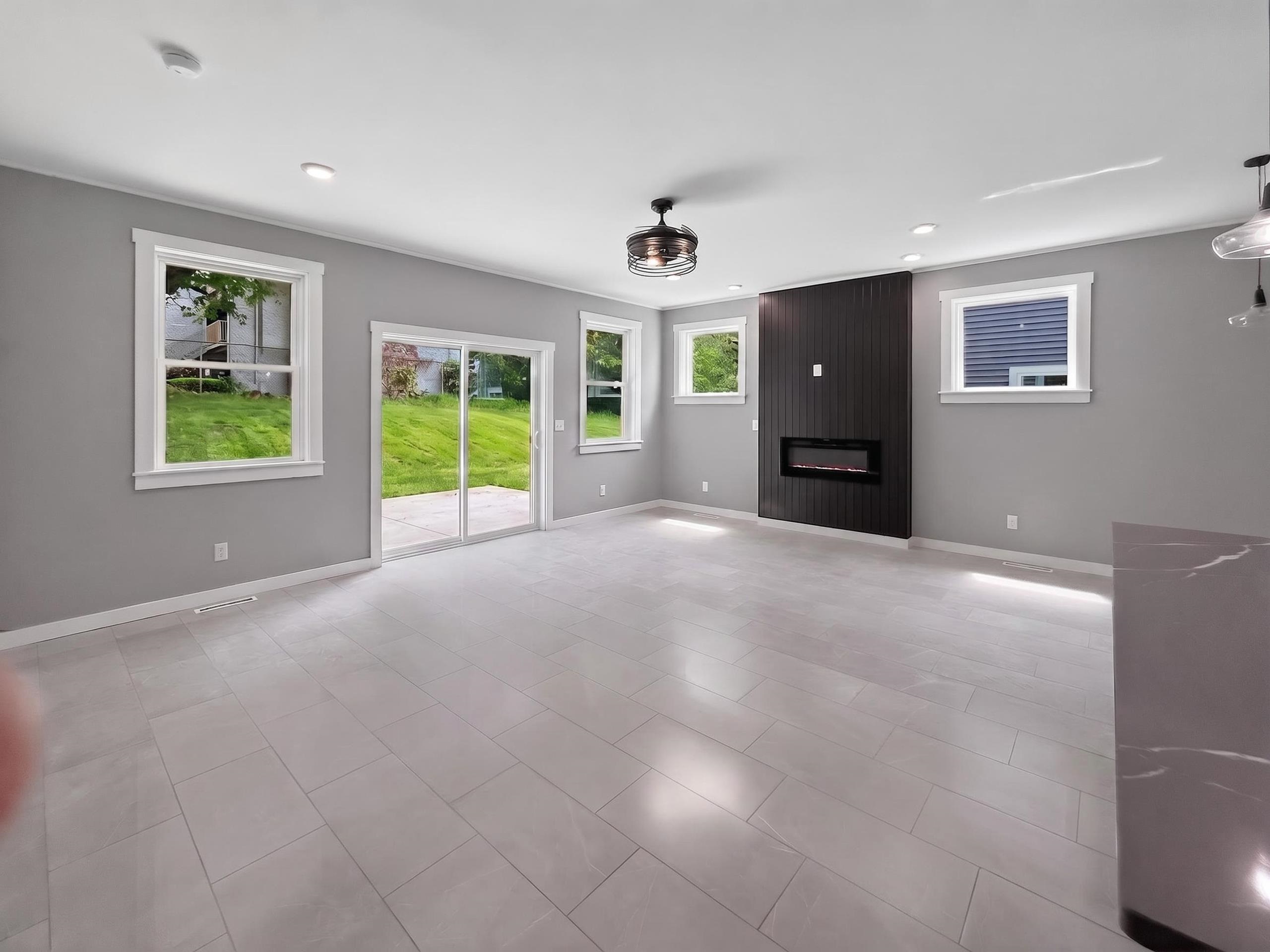 Spacious living area featuring light-toned tile flooring and a sleek electric fireplace with a dark wood-finish accent wall