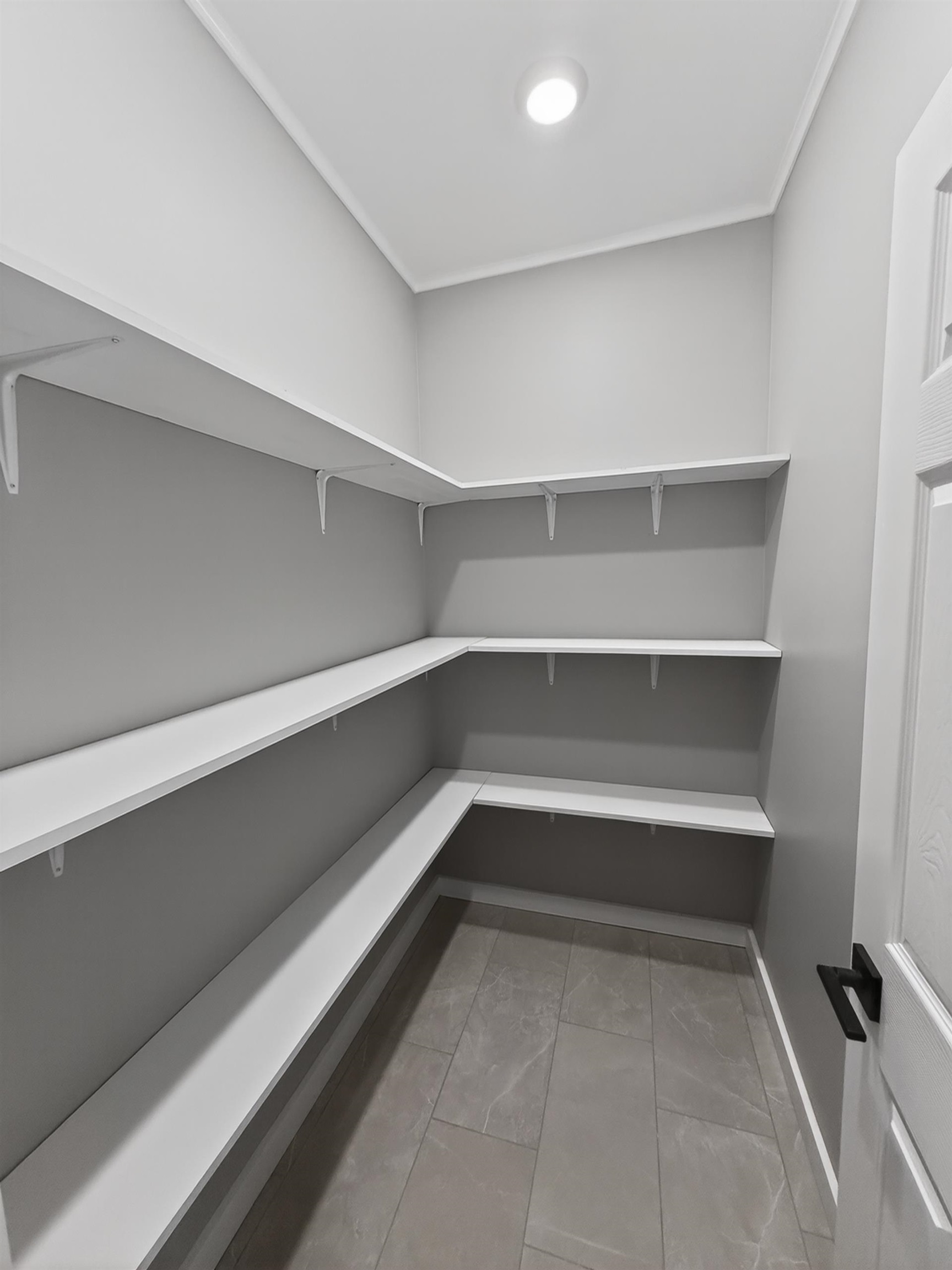 Walk-in pantry with ample white shelving, recessed lighting, and large format tile flooring