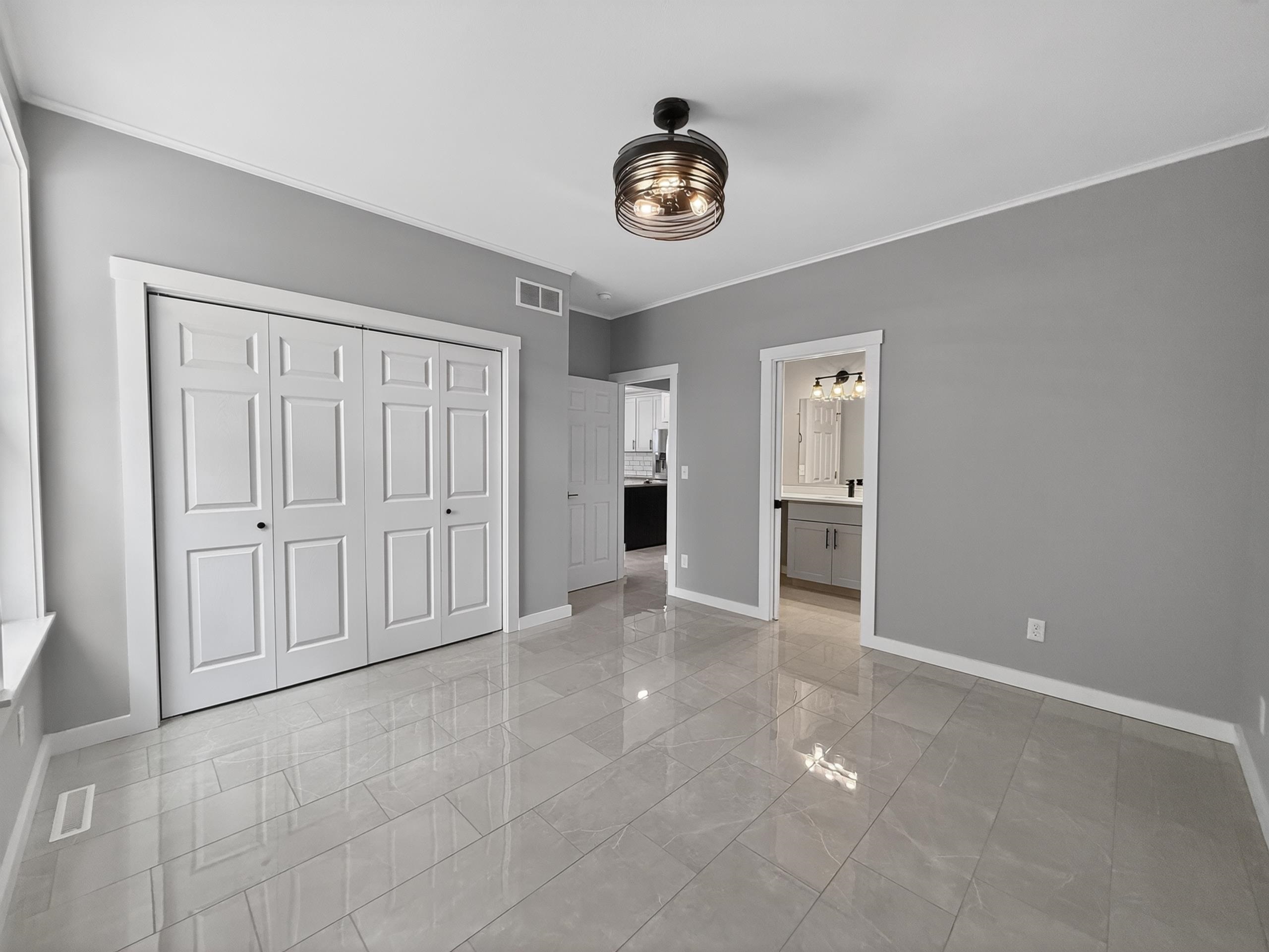Spacious room featuring light gray tile flooring, a contemporary ceiling light fixture, white trim, and bi-fold closet doors