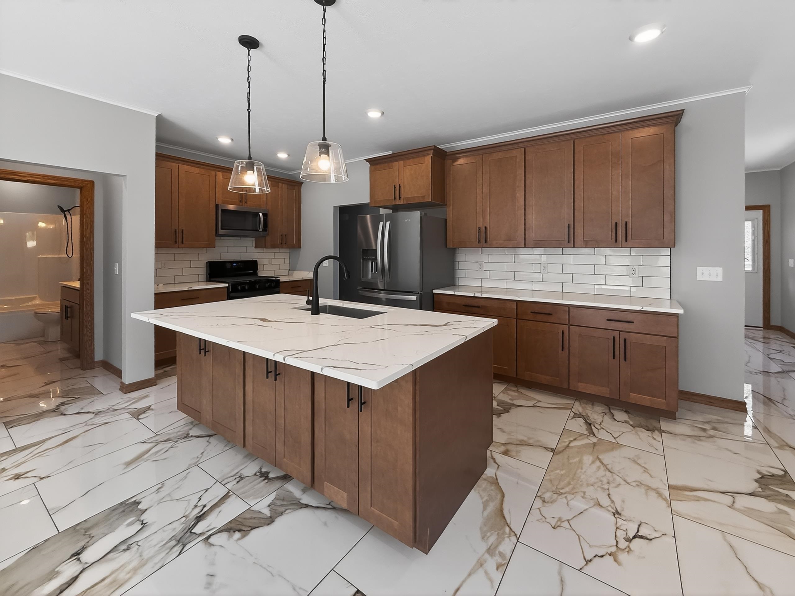 Kitchen featuring a central island with a stone-finish countertop, wood-finish cabinetry, subway tile backsplash, stainless steel appliances, and pendant lighting
