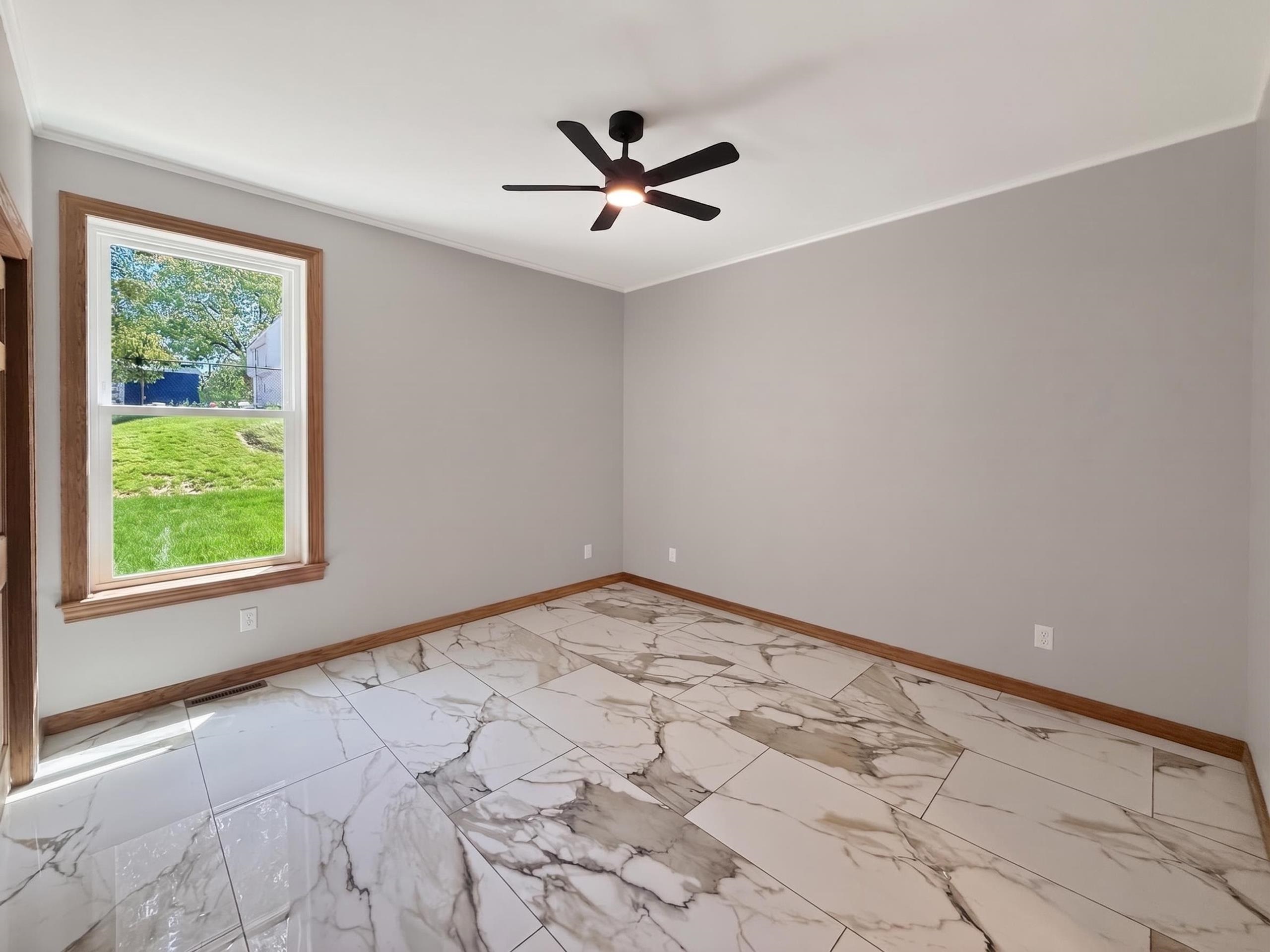 Spacious room featuring large format tile flooring, a contemporary ceiling fan, and natural wood trim around the window and baseboards