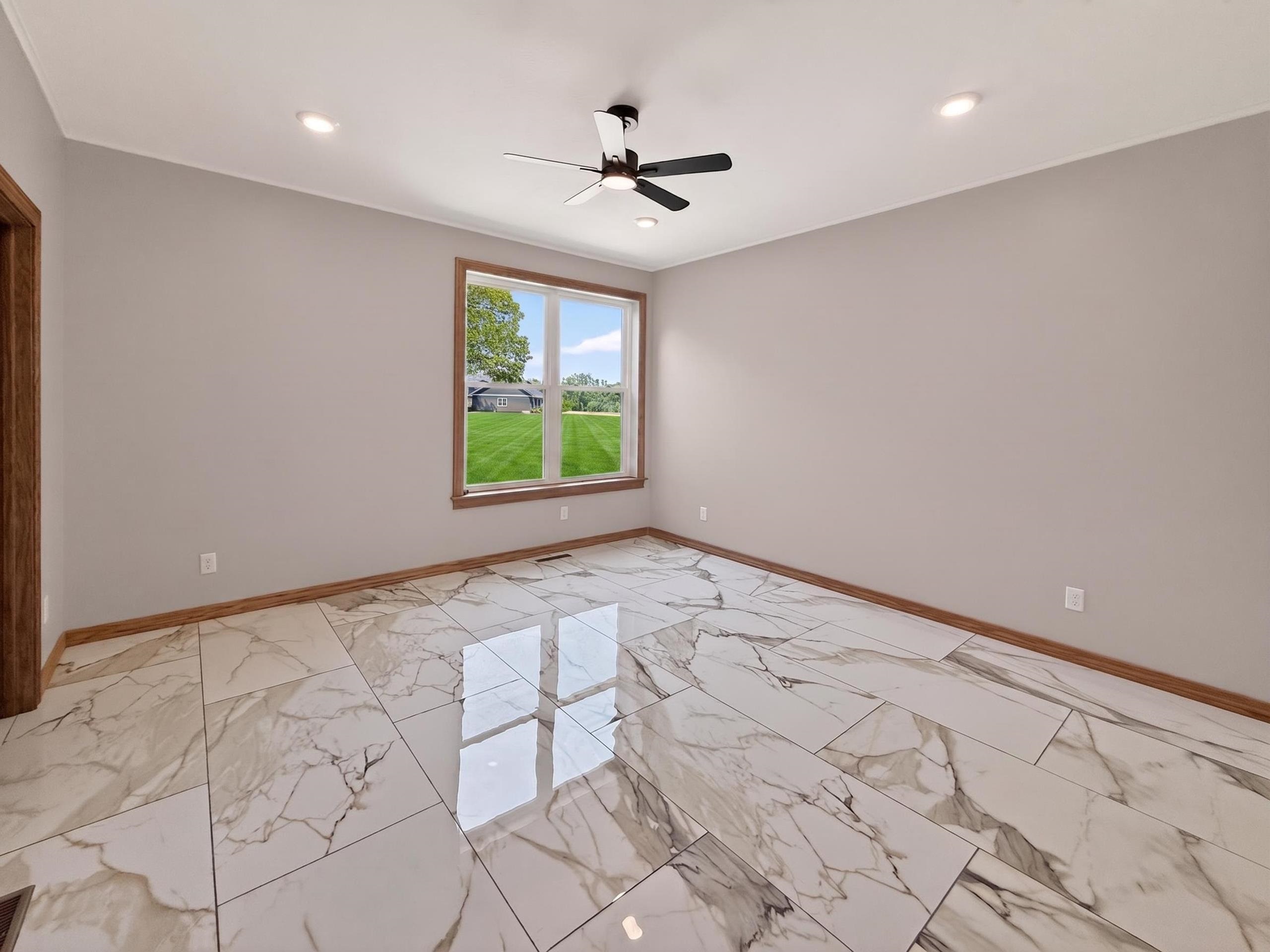 Spacious room featuring large format porcelain tile flooring, a ceiling fan with integrated lighting, recessed lighting, and a large window with wood trim