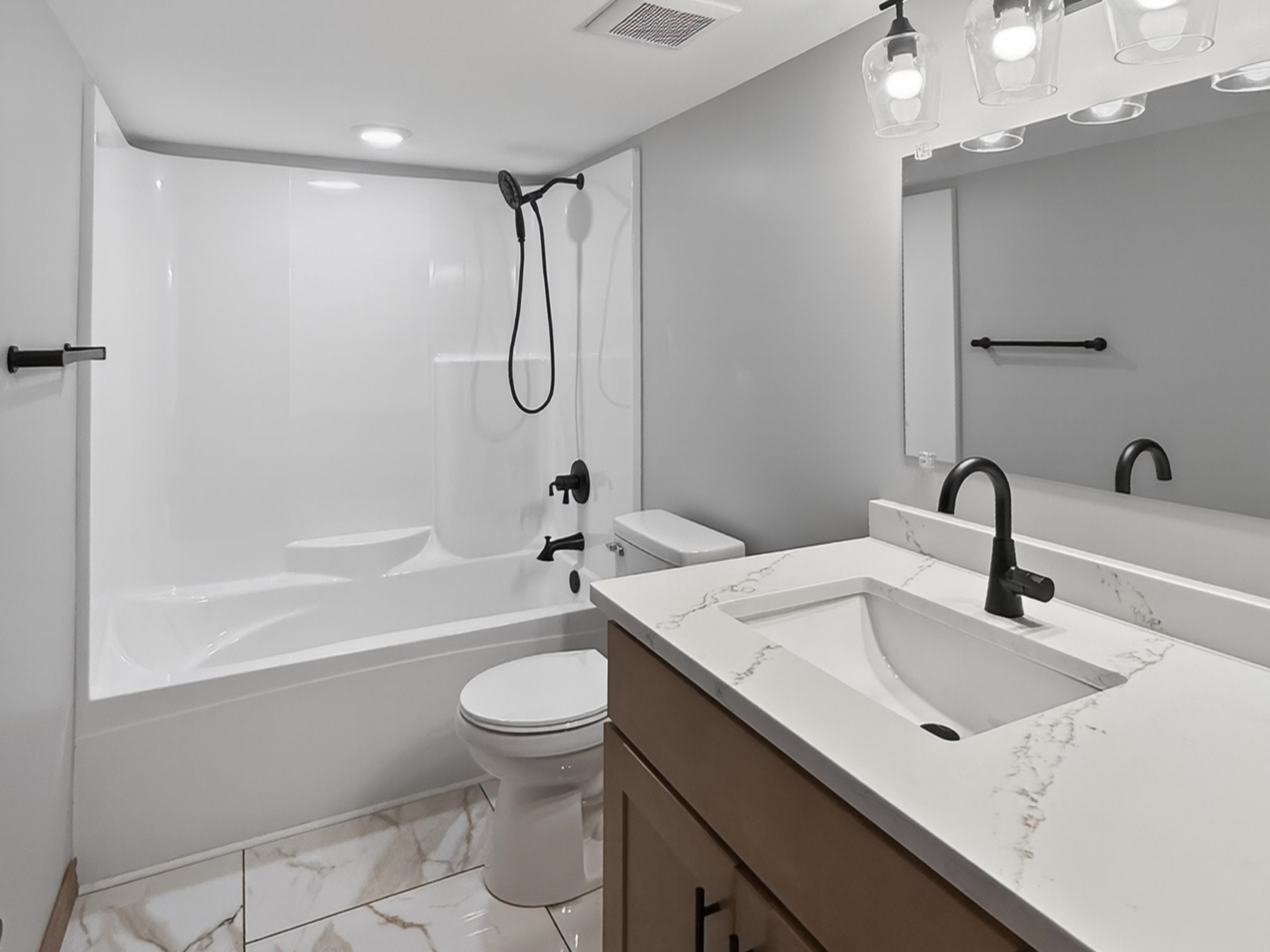 Bathroom featuring a white integrated tub and shower unit with matte black fixtures