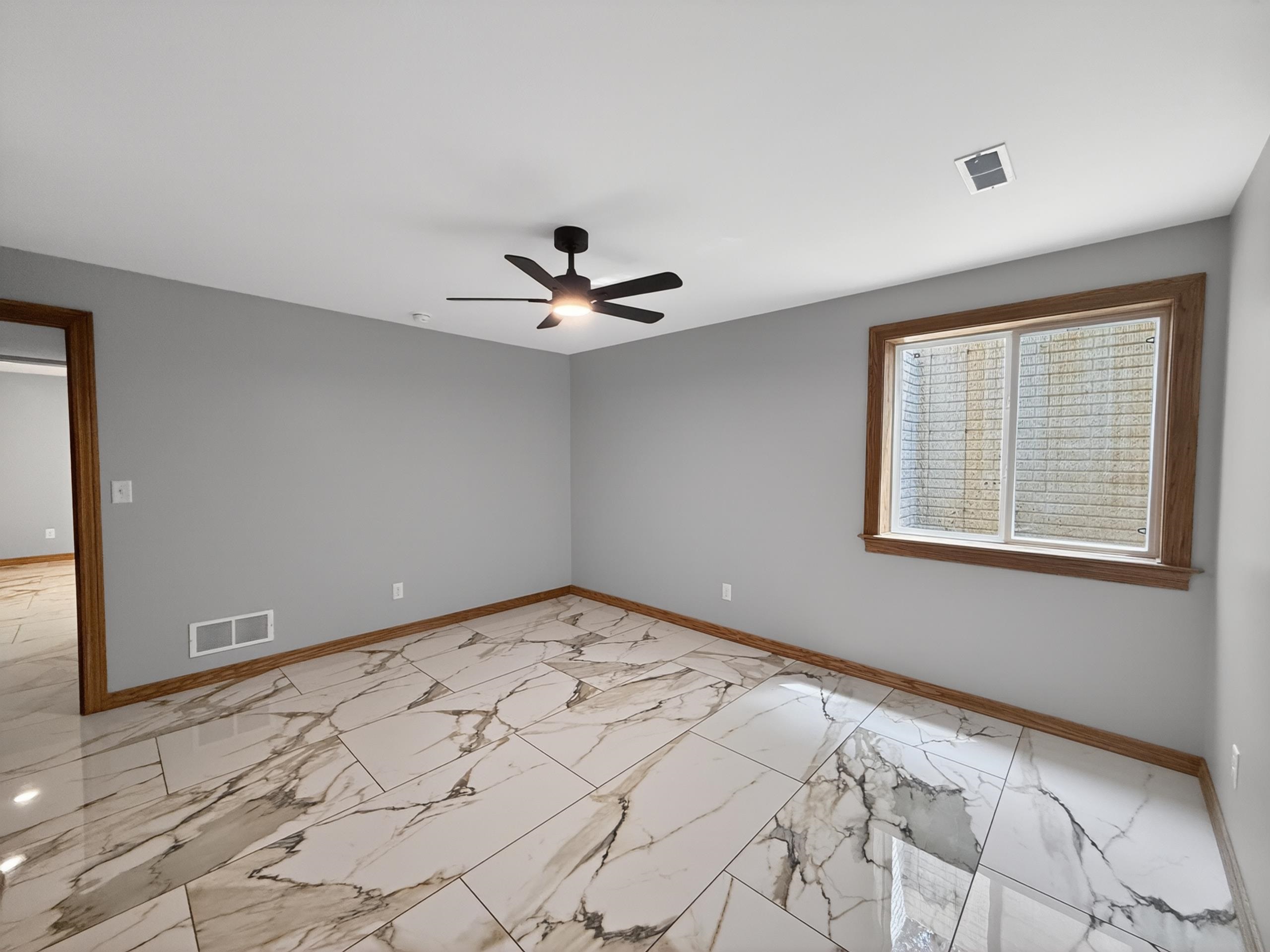 Spacious room featuring large format tile flooring with distinctive veining, light gray wall paint, and a dark-toned ceiling fan
