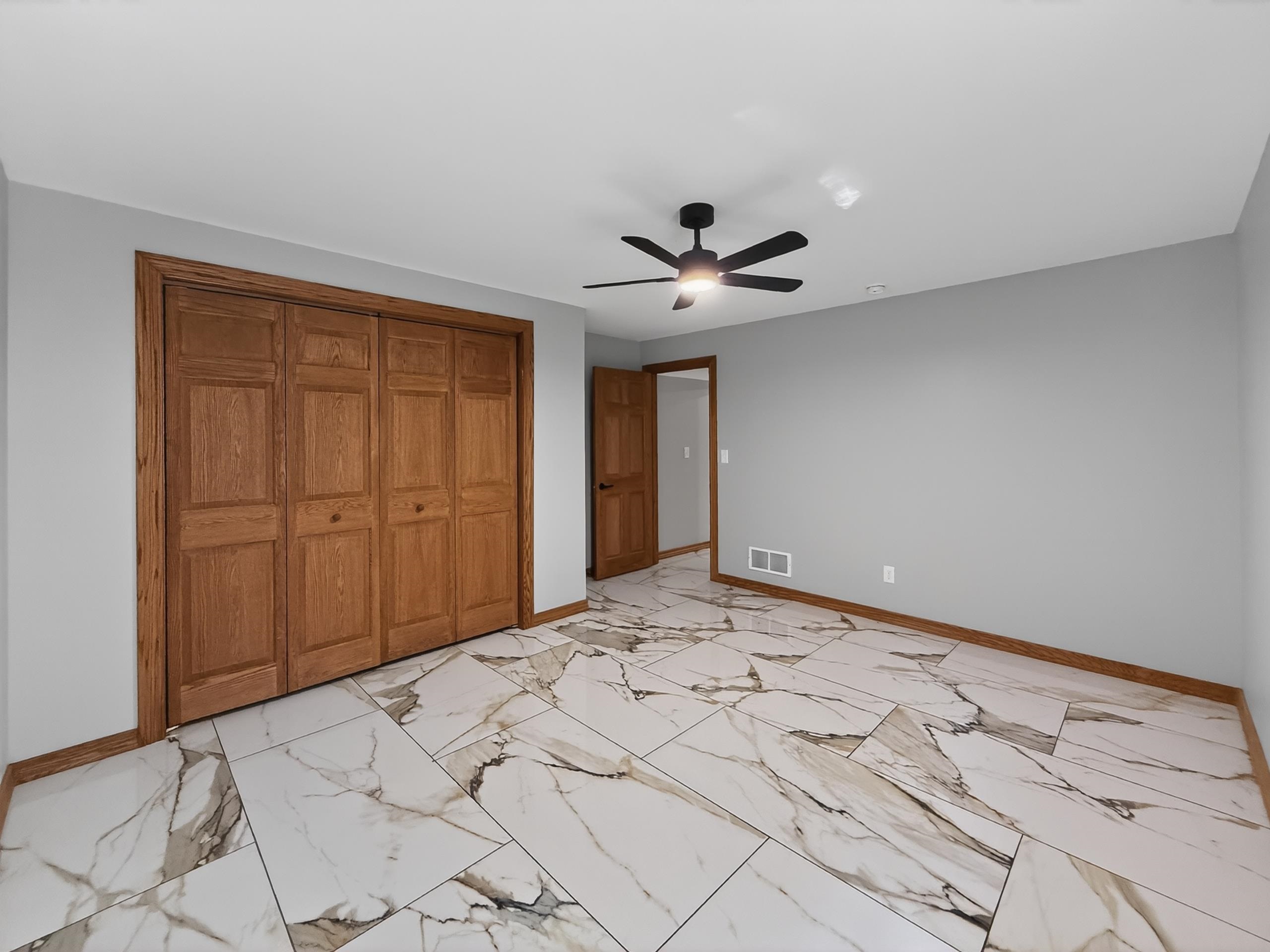 Spacious room featuring large format tile flooring with veining, light gray painted walls, and wood-finish bi-fold closet doors