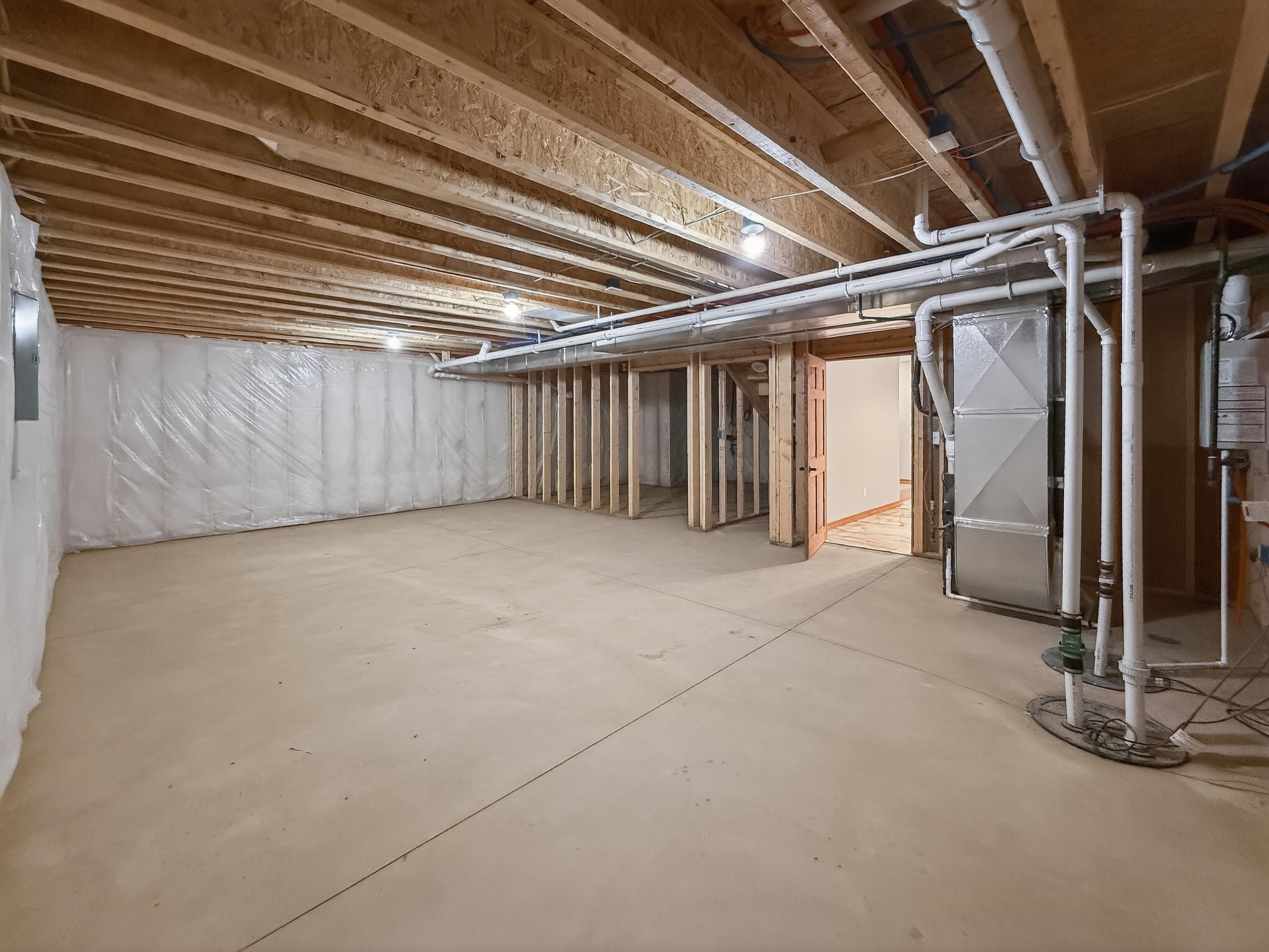 Unfinished basement with concrete flooring, exposed wood joists, and insulated perimeter walls