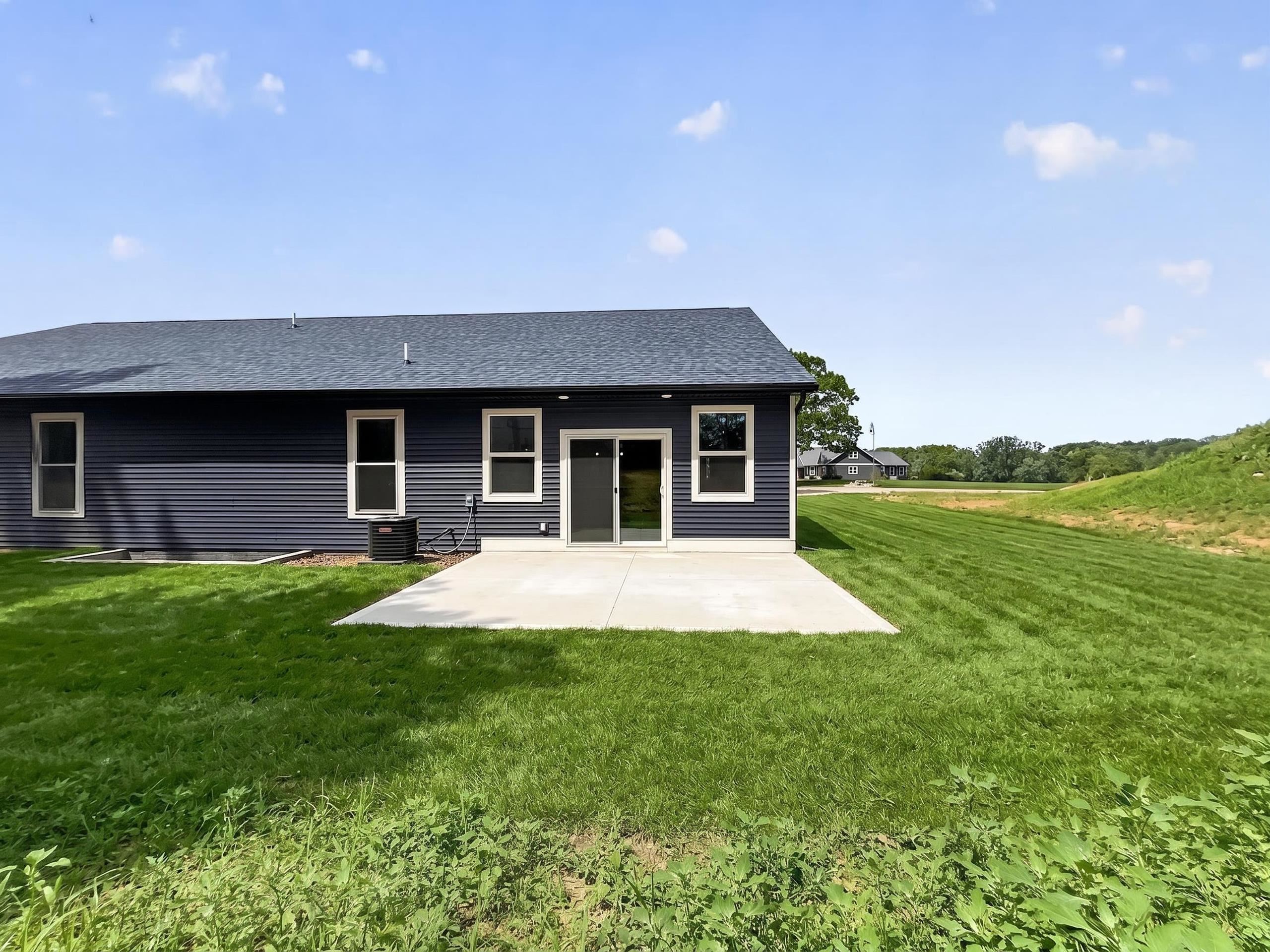 Rear exterior featuring dark horizontal siding, white trim windows, a concrete patio, a sliding glass door, and a shingled roof