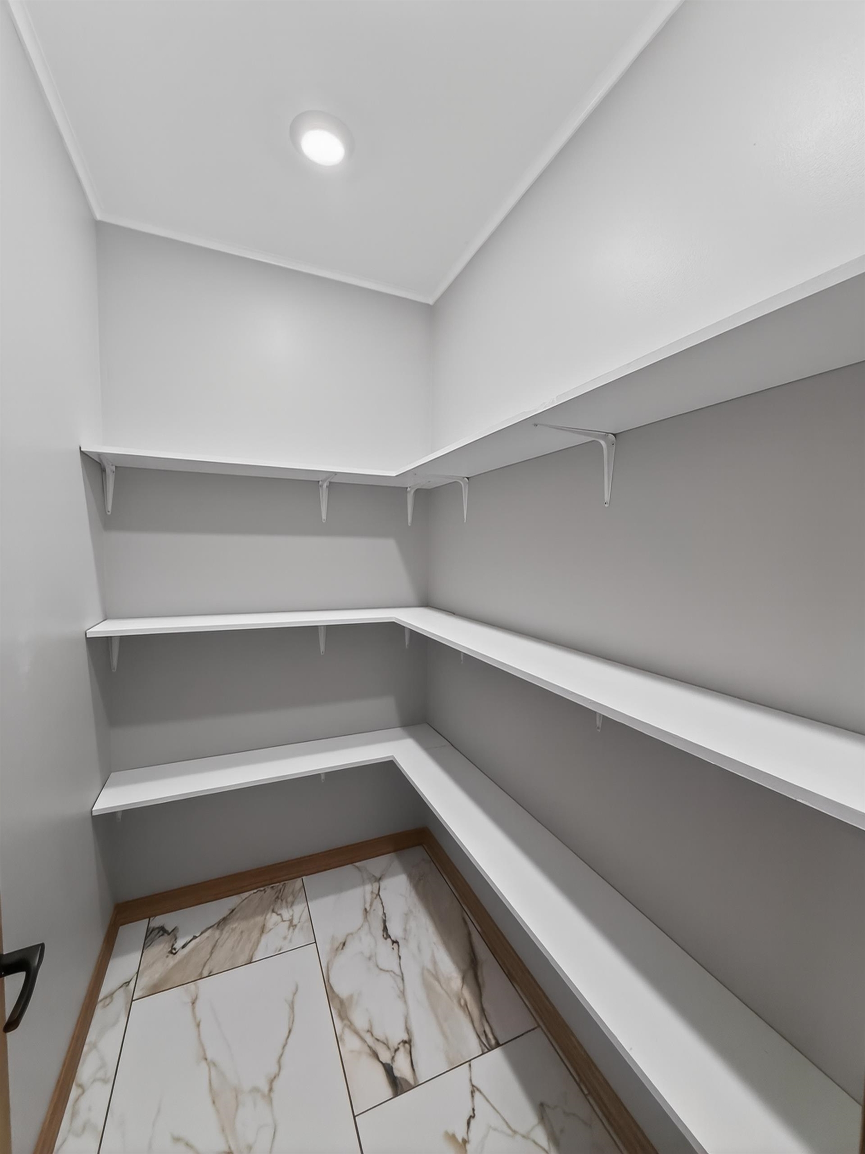 Walk-in pantry featuring white shelving, light gray walls, recessed ceiling lighting, and large format tile flooring with a wood-finish perimeter