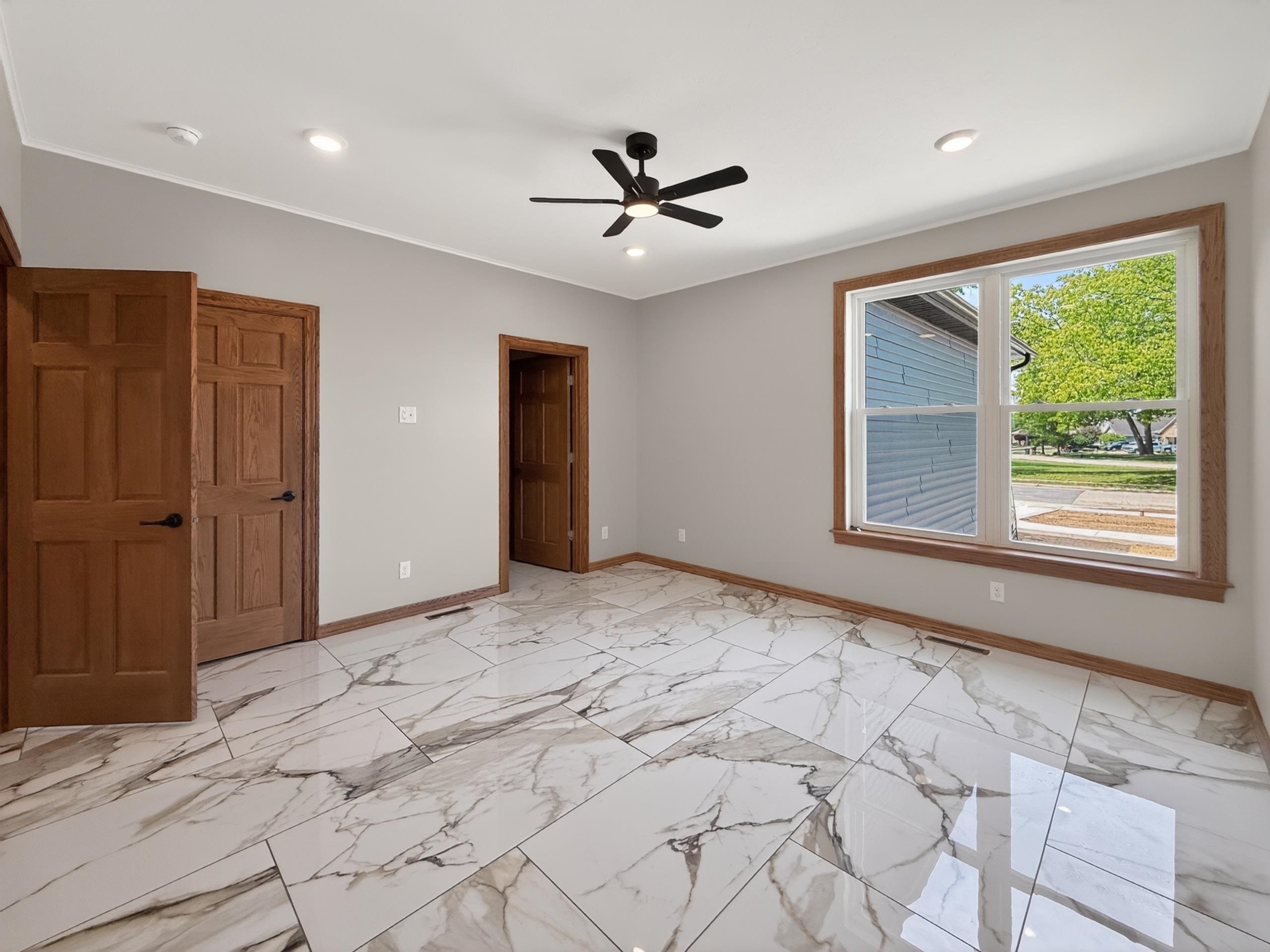 Spacious room featuring large format marble-look tile flooring, light gray wall paint, and warm wood-finish trim and doors