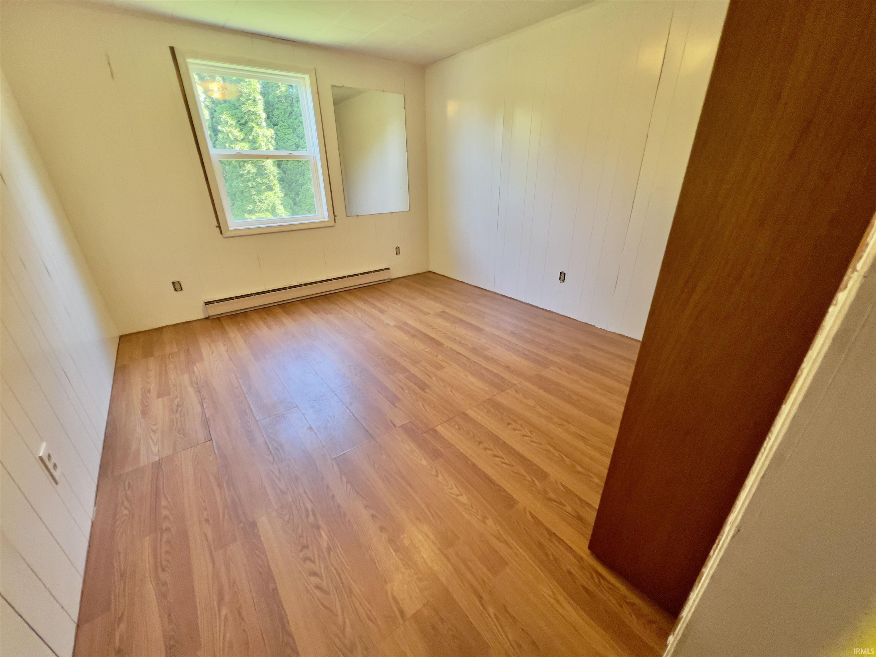 Room featuring wood-finish flooring, a double-hung window and white vertical paneling on one wall.