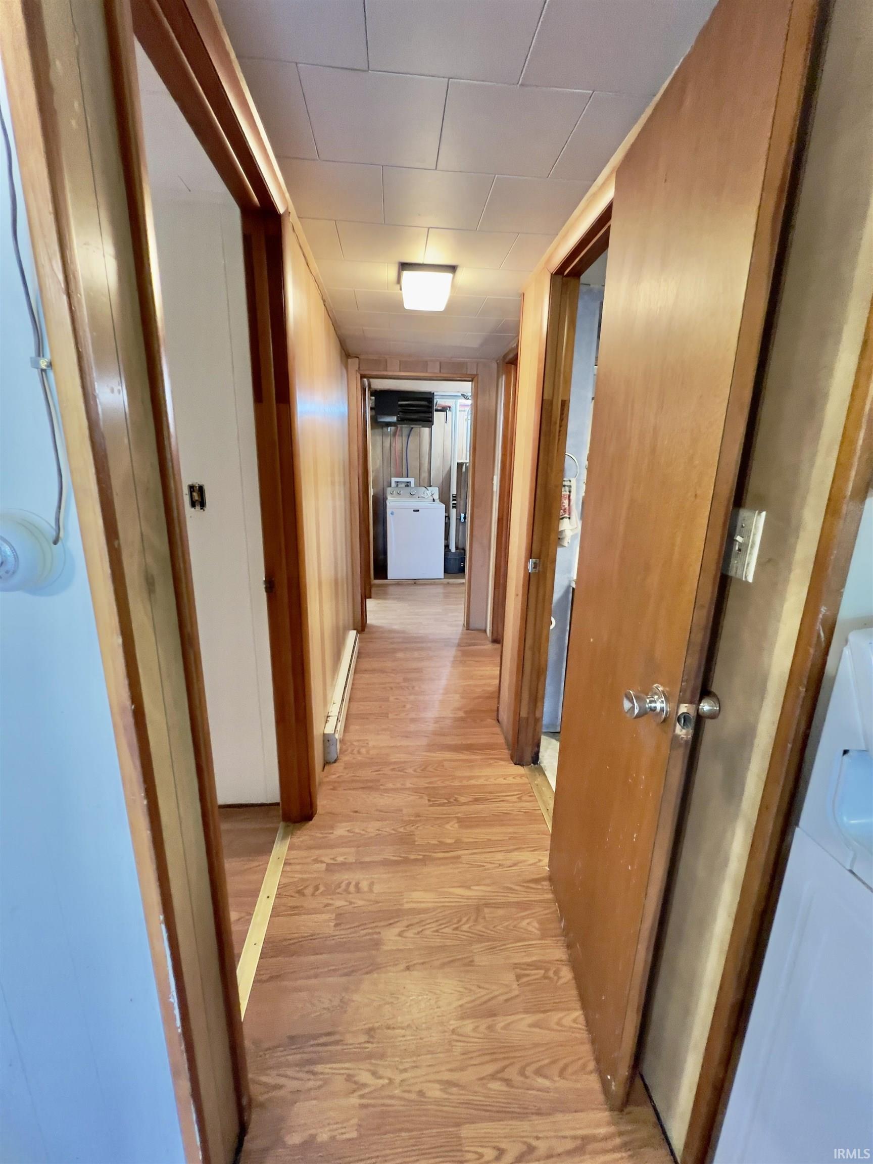 Hallway featuring wood-finish flooring, light wood paneling, multiple doorways, and a flush-mount ceiling light fixture