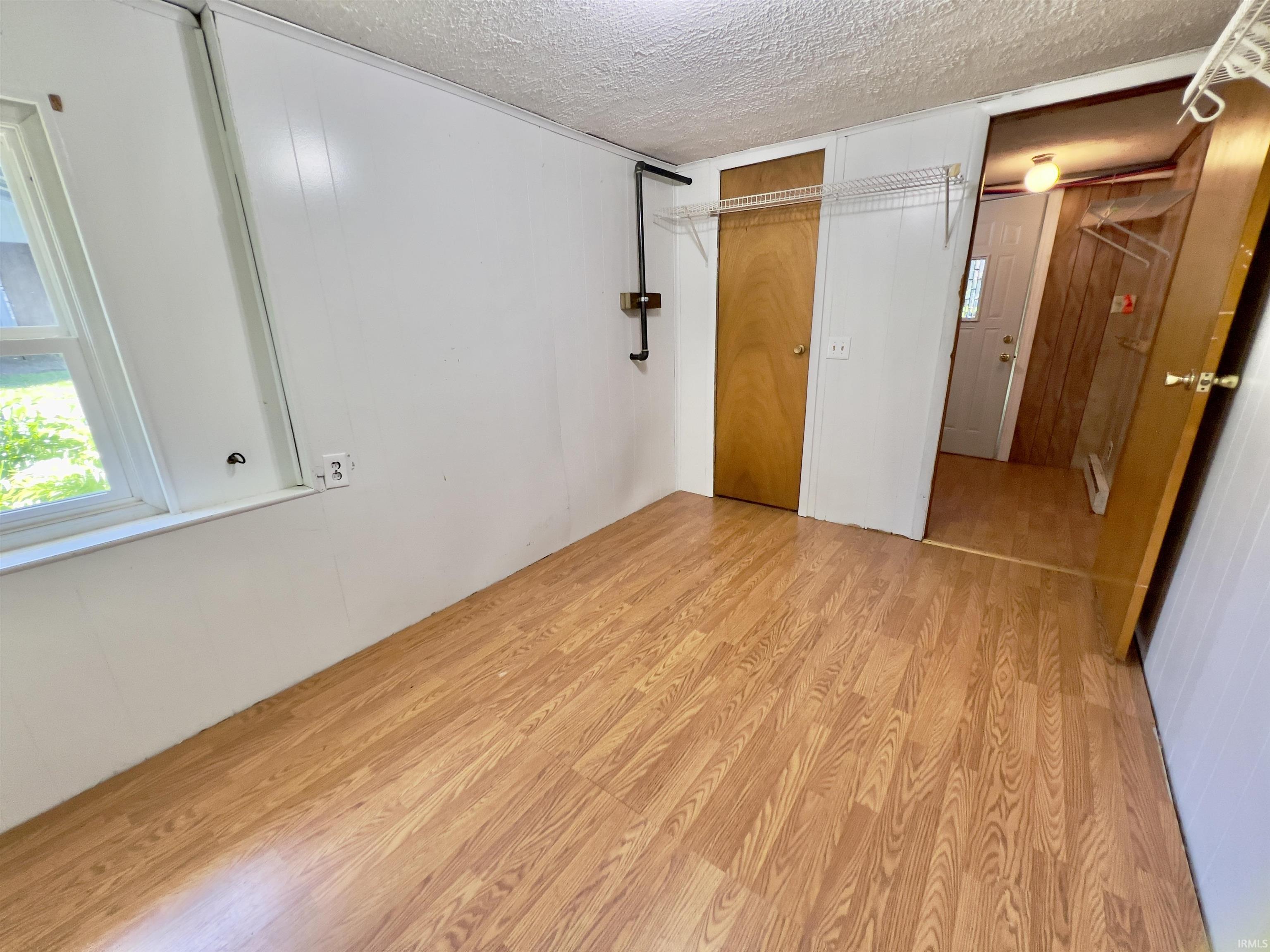 Room with wood-finish flooring, white panel walls, and a window