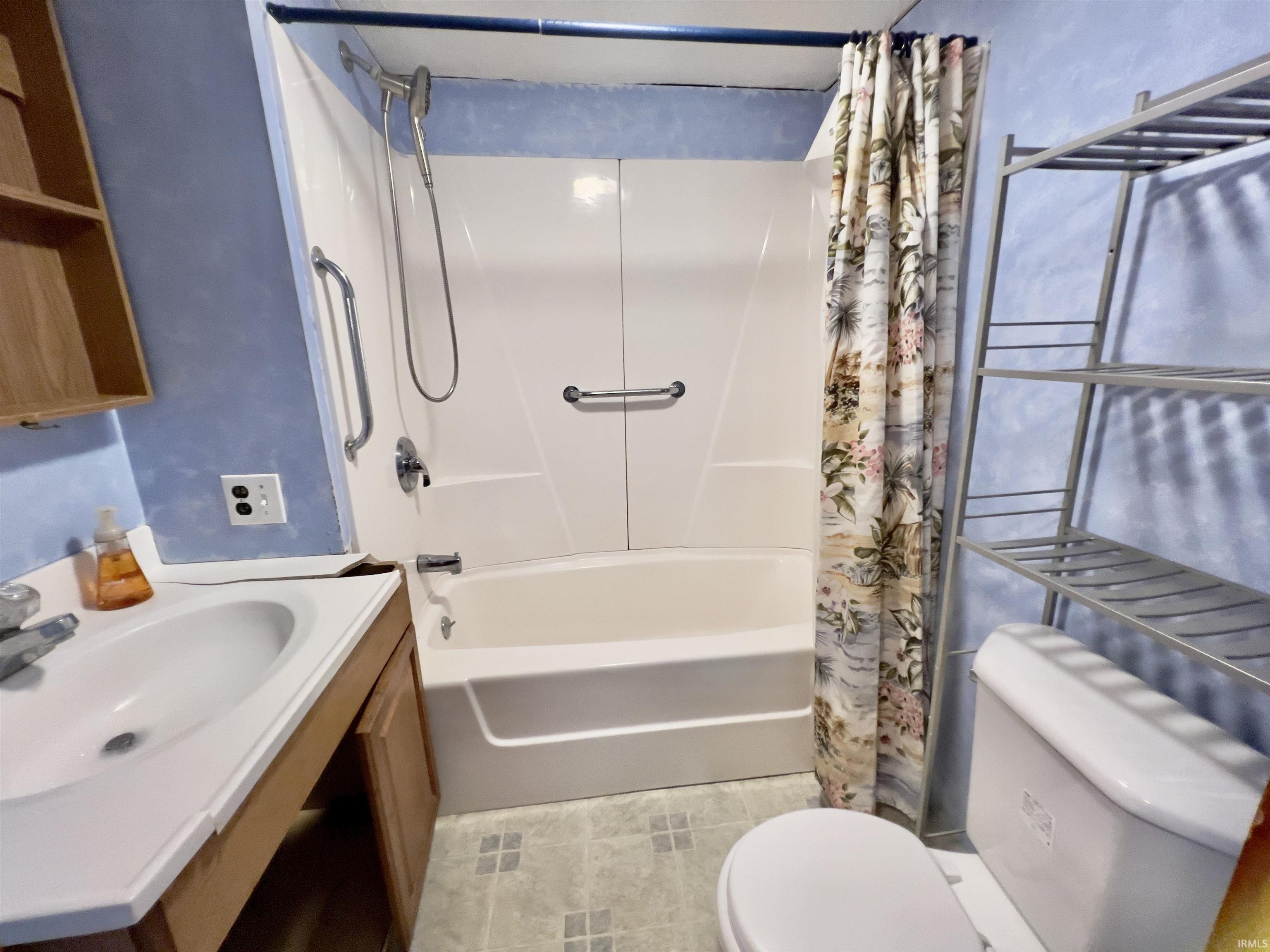 Bathroom featuring a white tub-shower combination unit, a single vanity, a toilet, and light-toned floor tiles