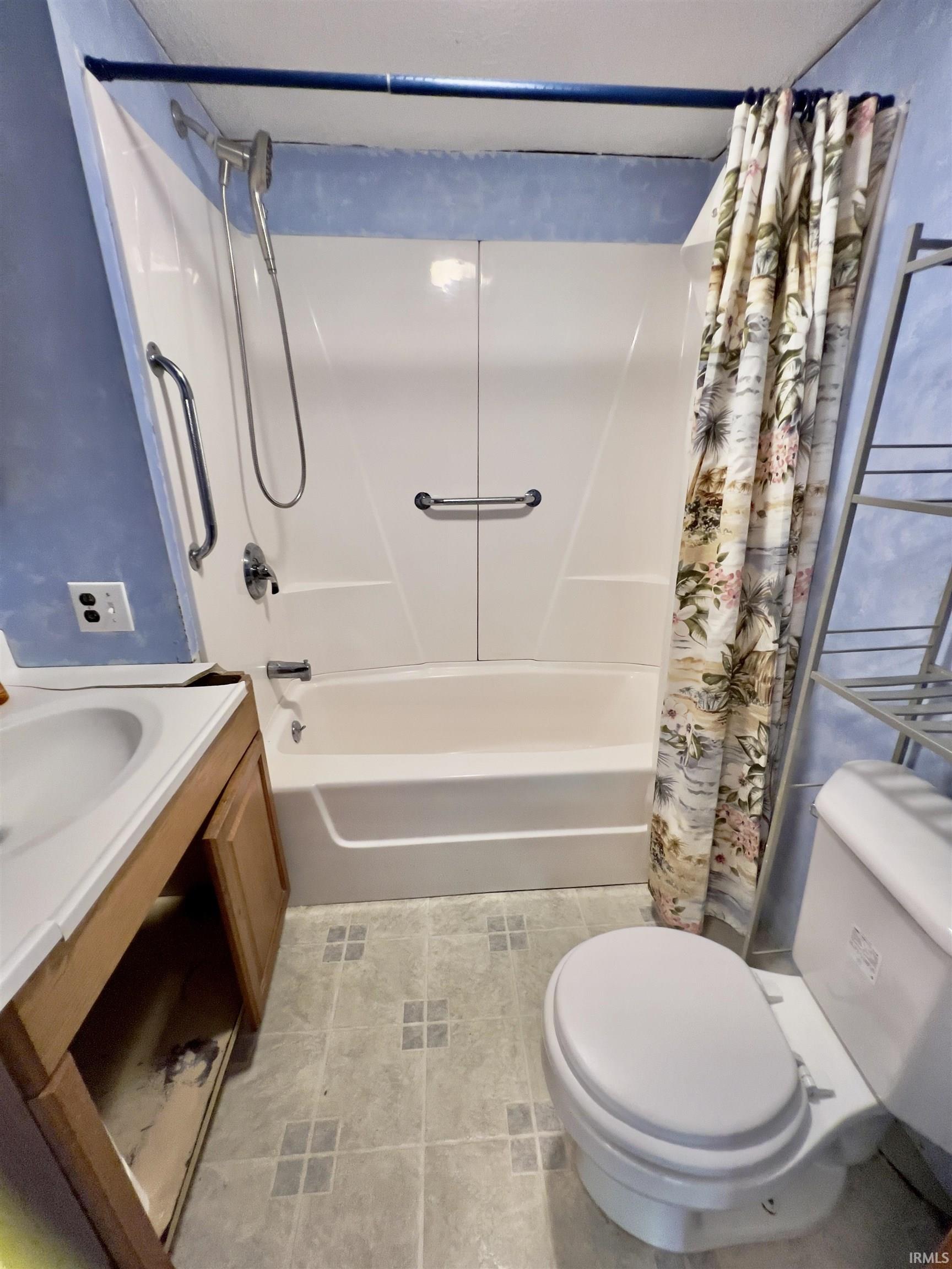 Bathroom featuring a white tub and shower surround with dual grab bars