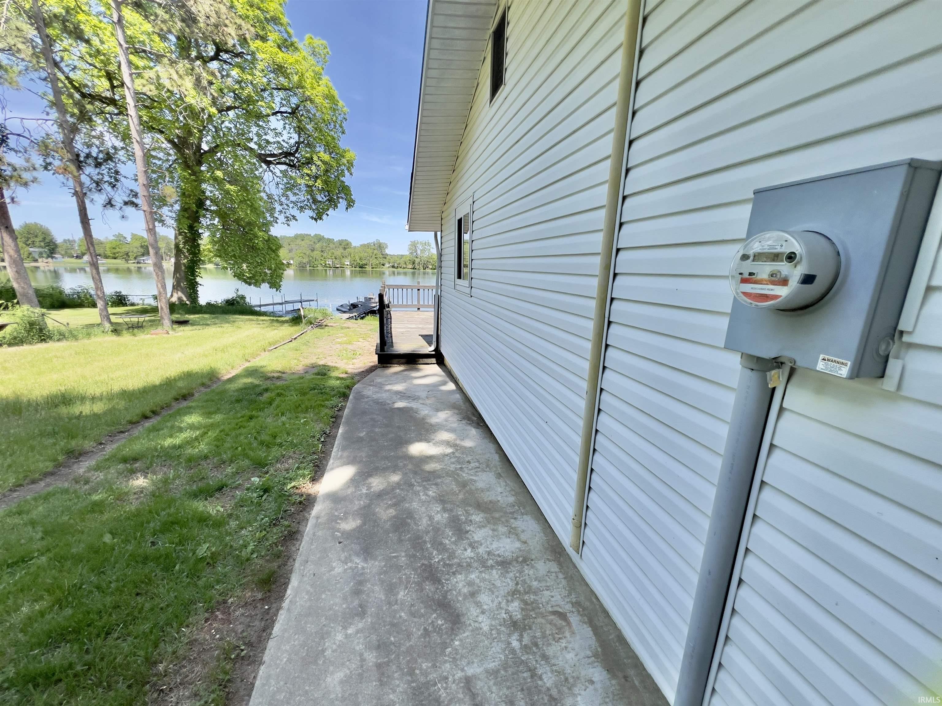 Waterfront property featuring a white vinyl-sided exterior, a concrete walkway, and a wooden deck overlooking the water