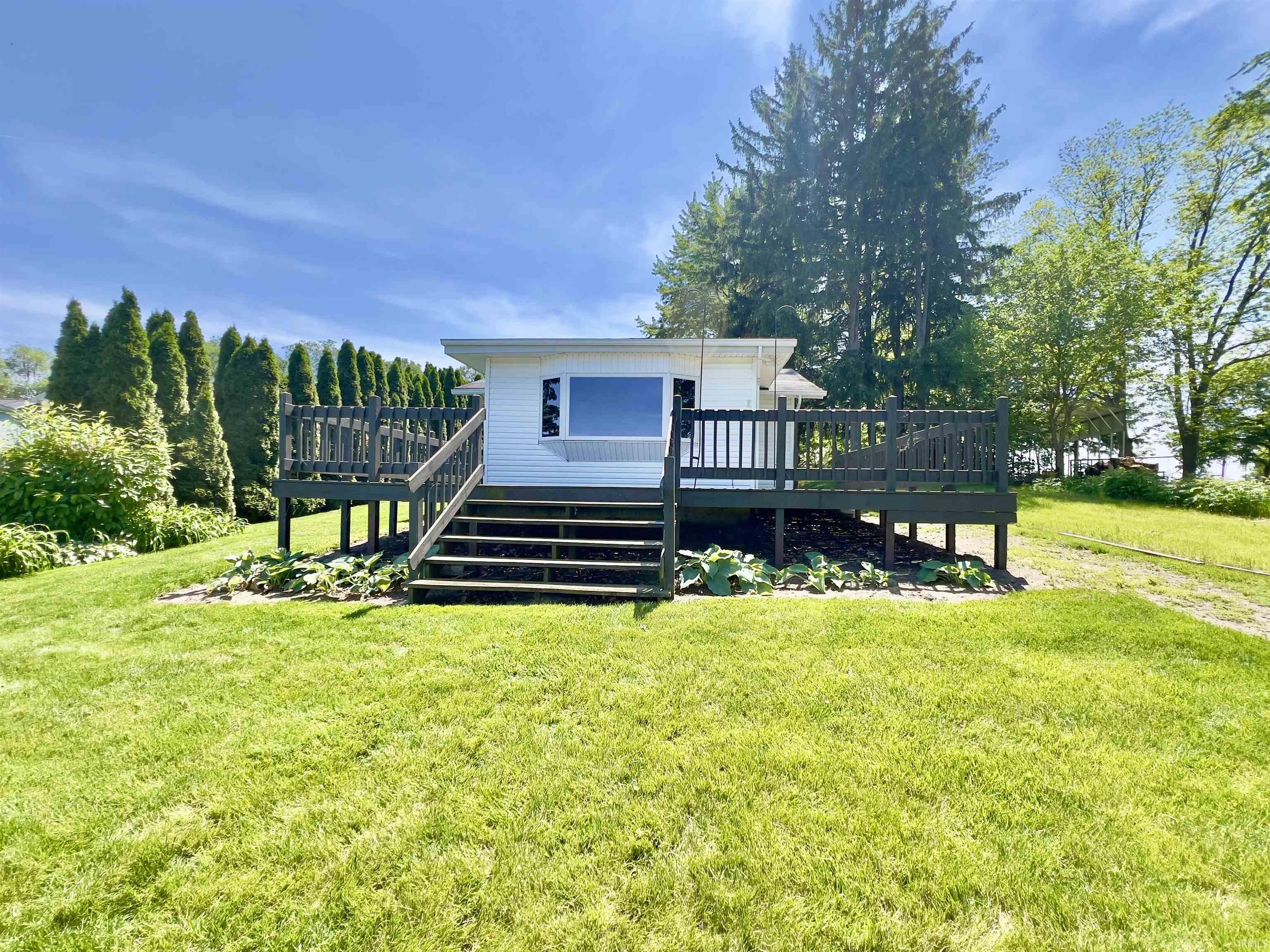 White exterior with dark-stained elevated deck and stairs featuring a large bay window.