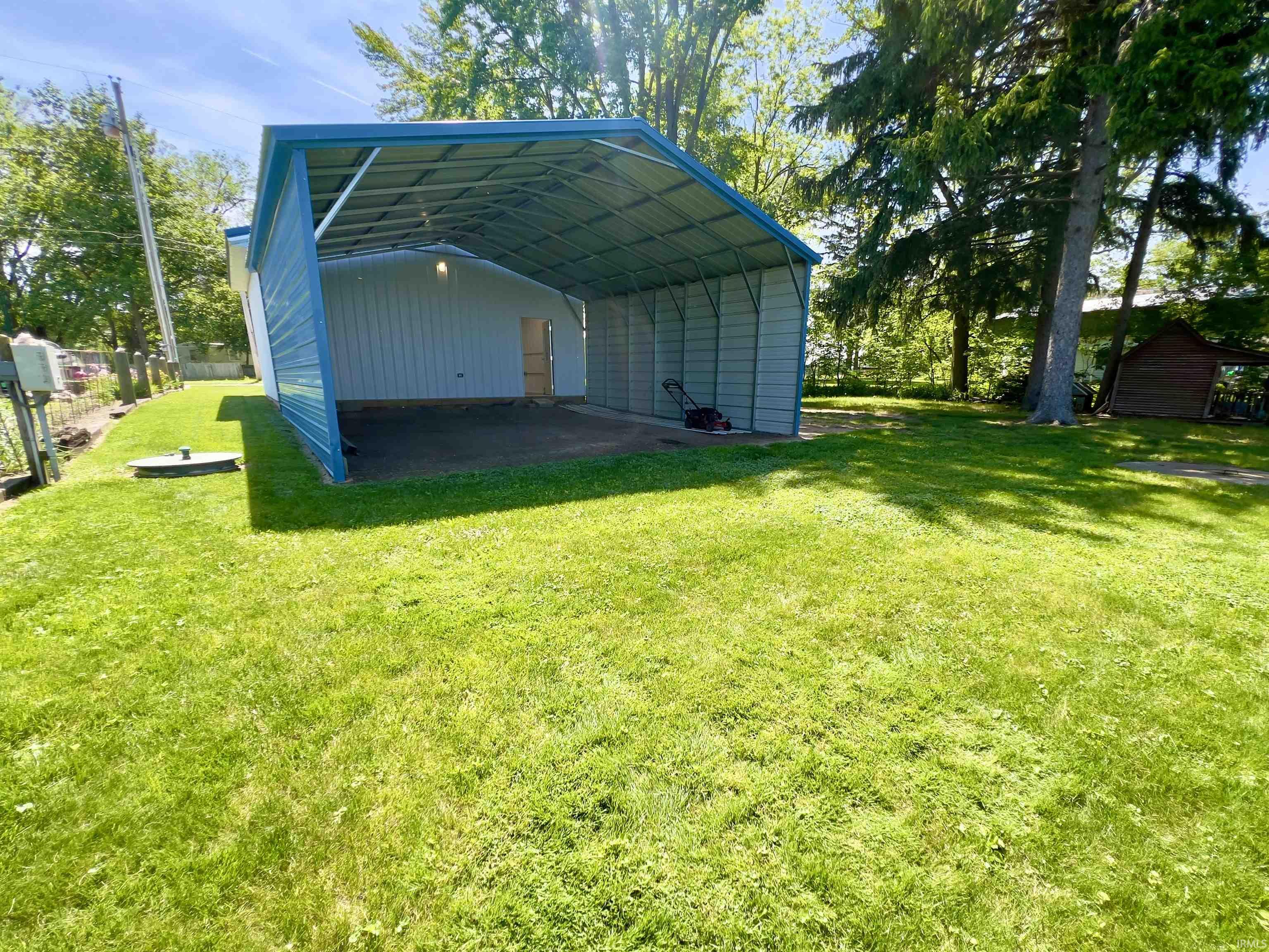 Open-sided carport structure featuring a blue metal roof and siding, concrete flooring, and a rear door