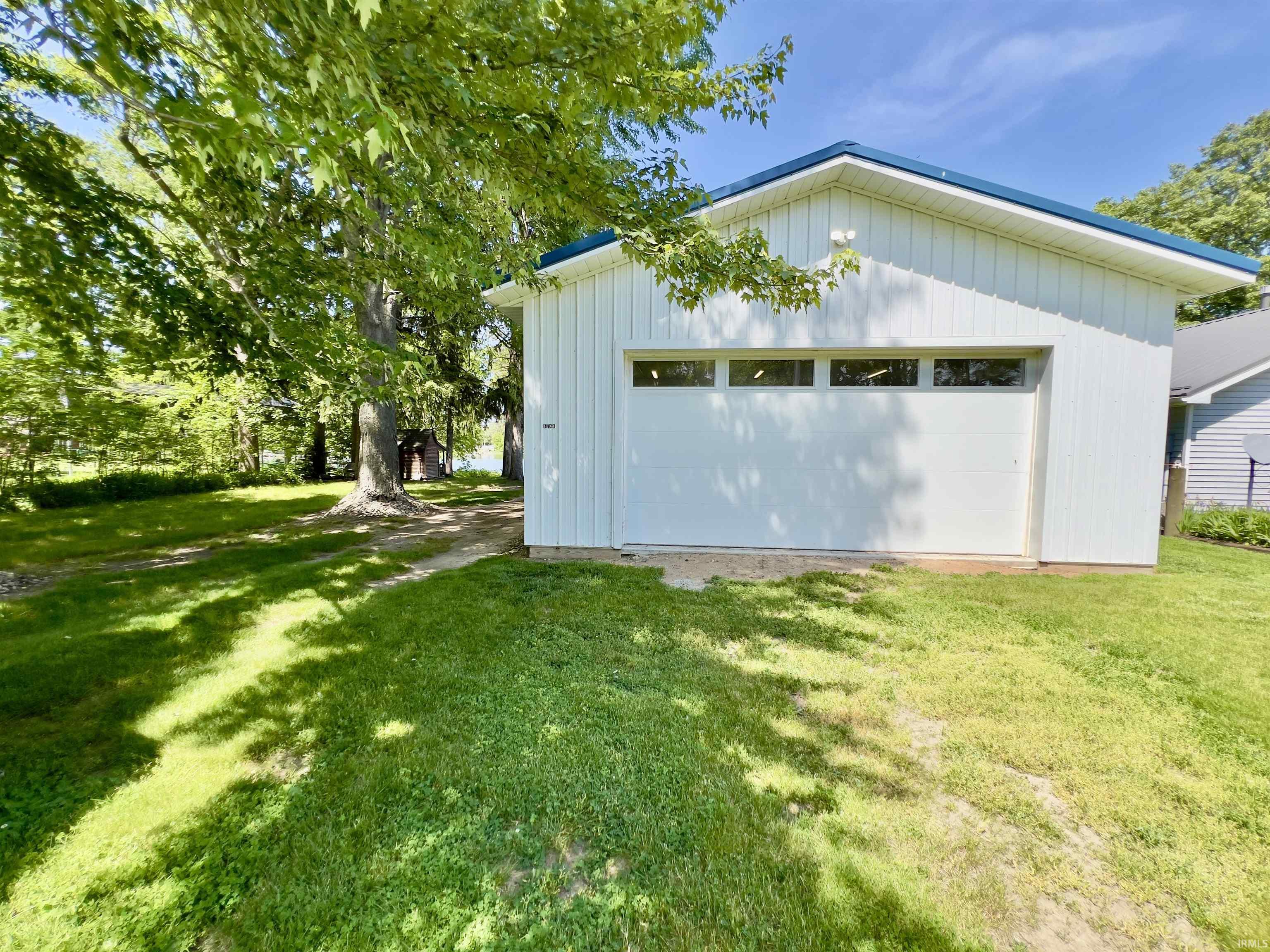 Detached white garage featuring a dark blue roof, horizontal window accents, vertical siding, and a white overhead door