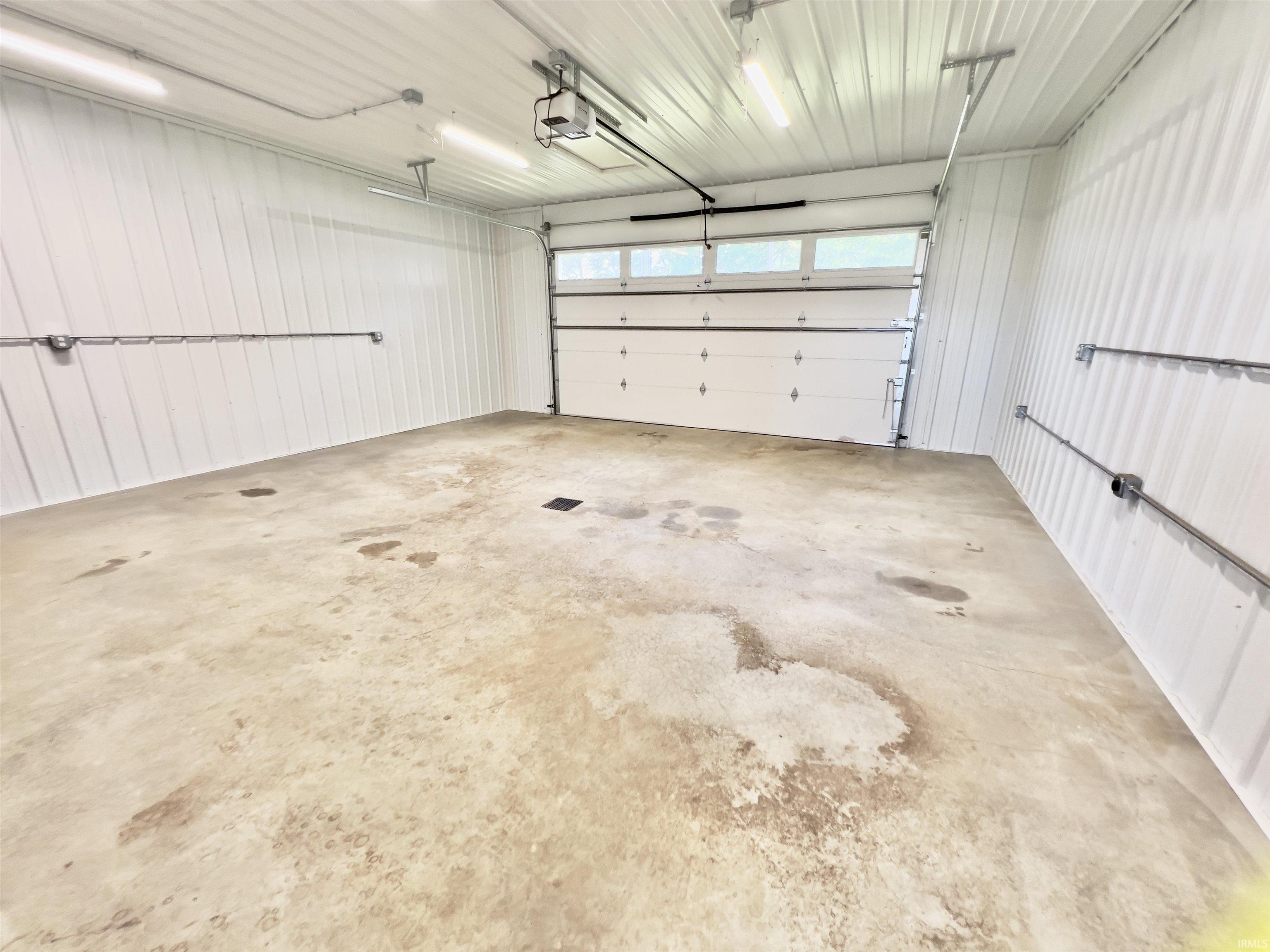 Spacious garage with a concrete floor, white corrugated metal walls, and a white paneled garage door with upper light panels