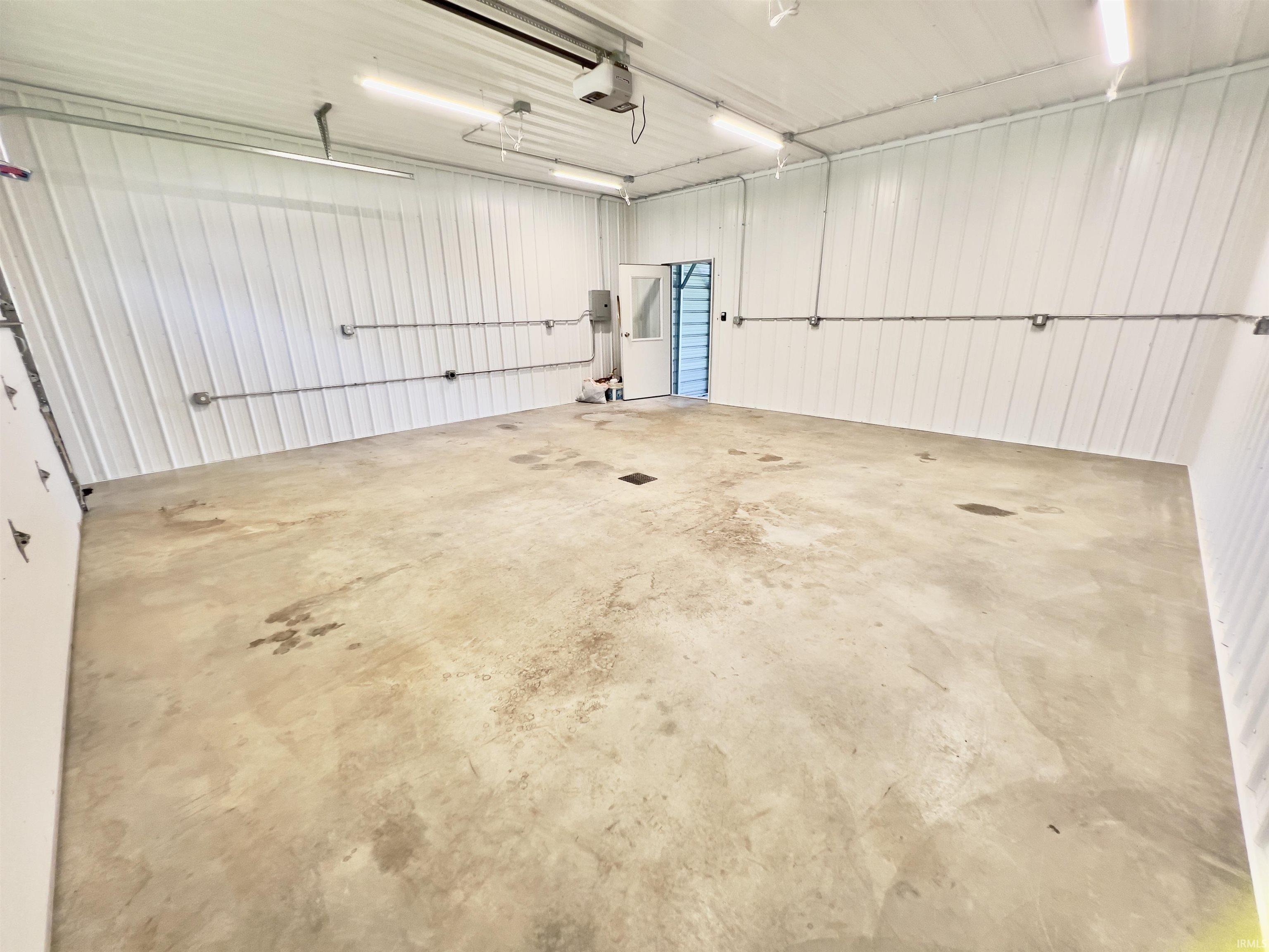 Spacious interior features a concrete floor, corrugated metal walls, and overhead lighting